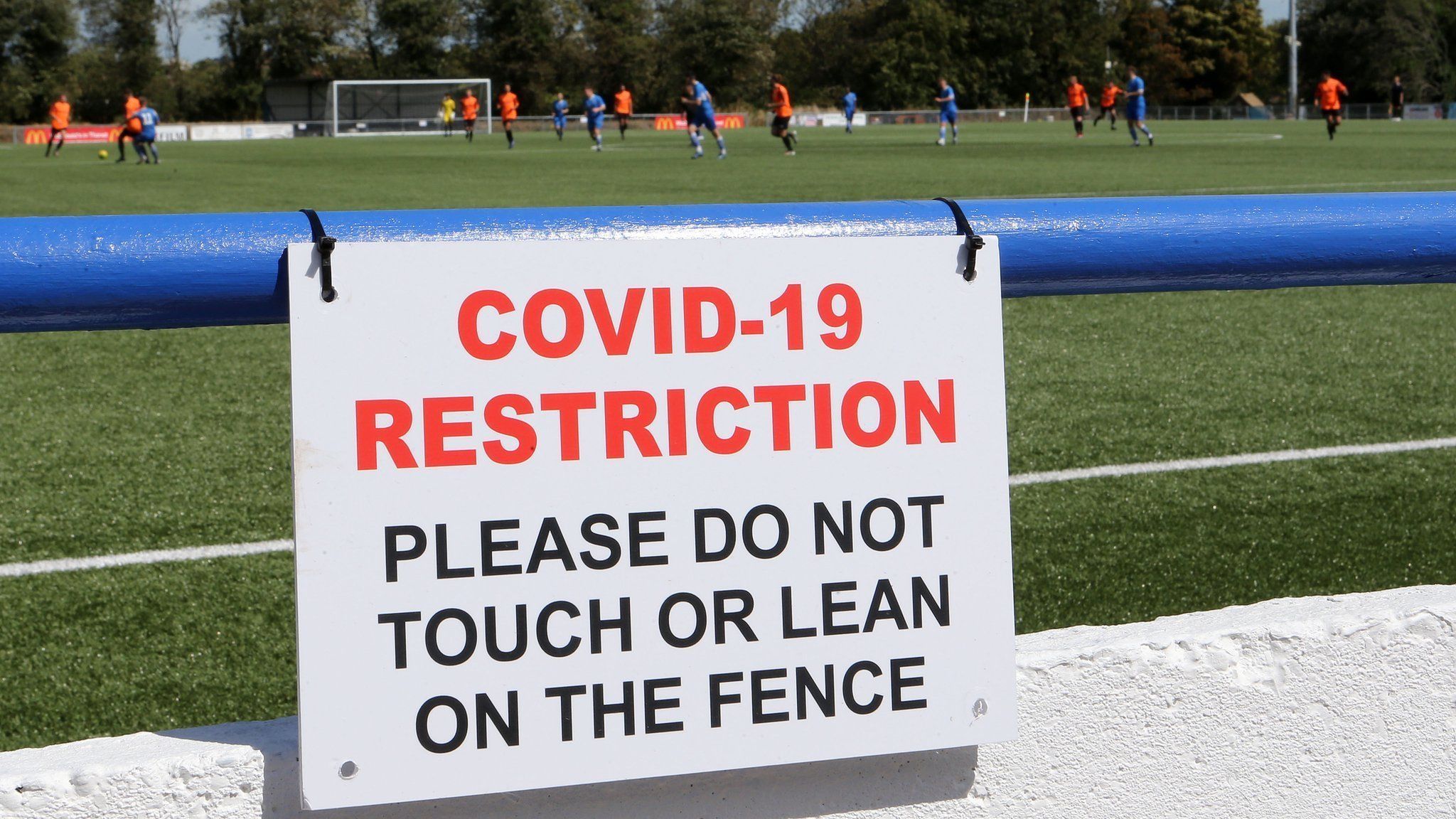 A Covid-19 restriction sign advising fans not to touch or lean on the fence as fans return to non-league football