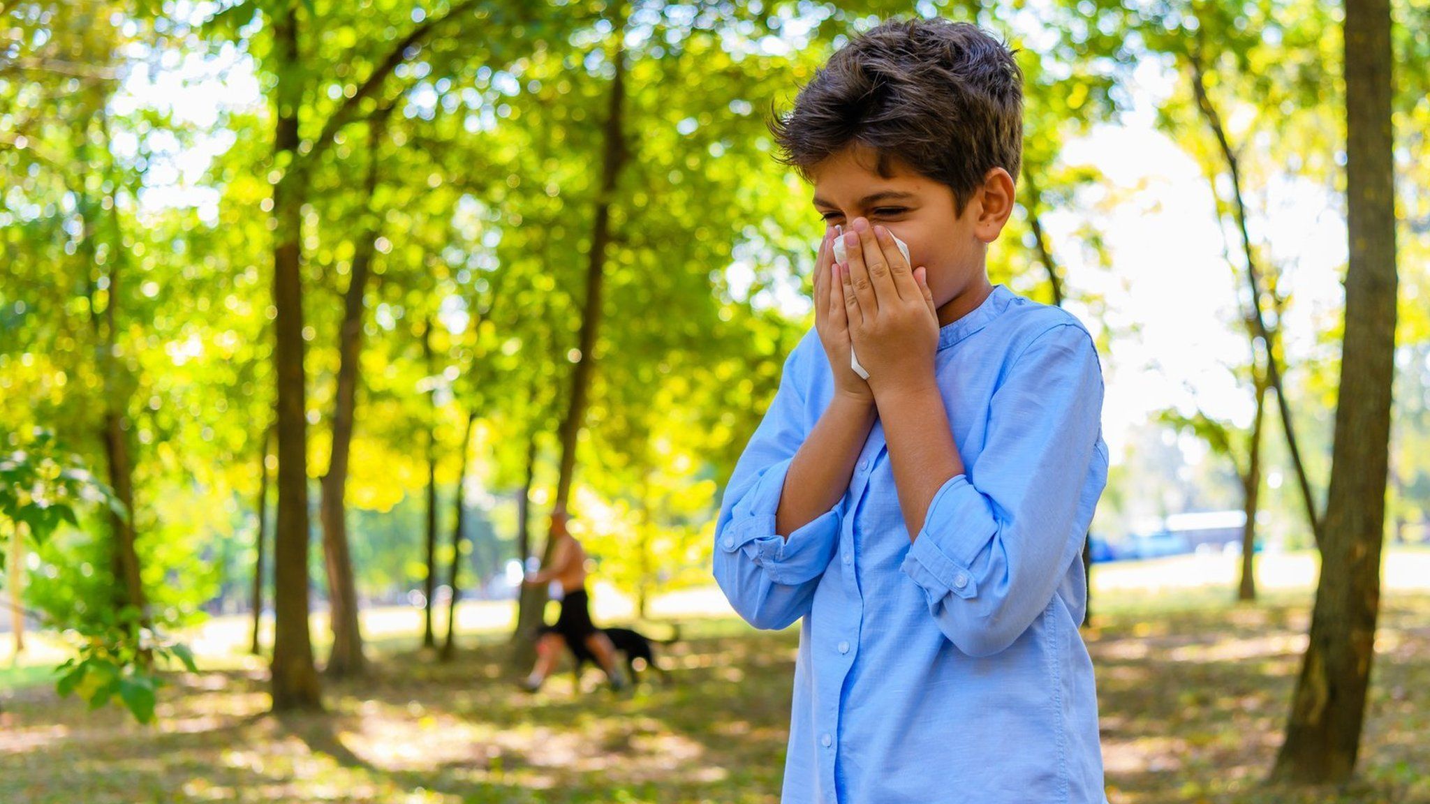 Boy standing in forest blows nose