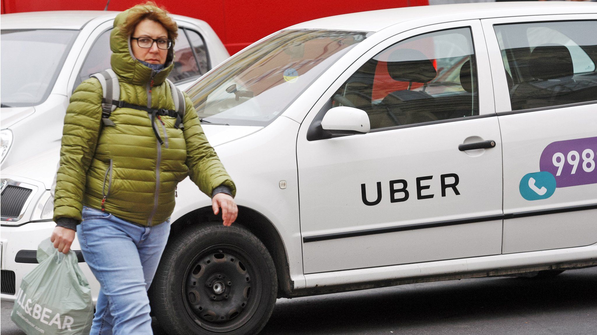 A woman seen walking next to a white car with a logo of Uber taxi cab company in Kiev, Ukraine.