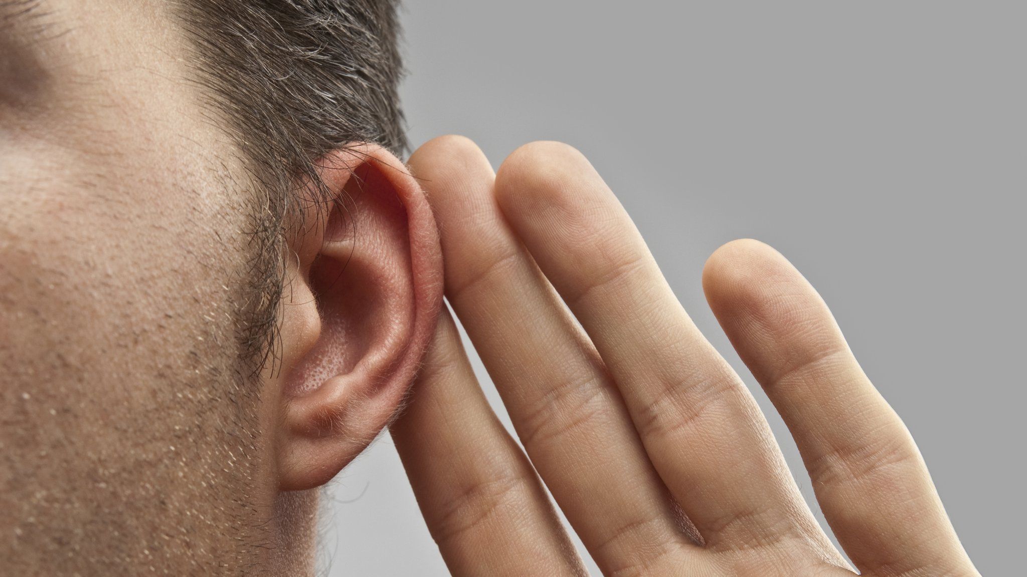 A close up of a man holding his left hand up to his left ear