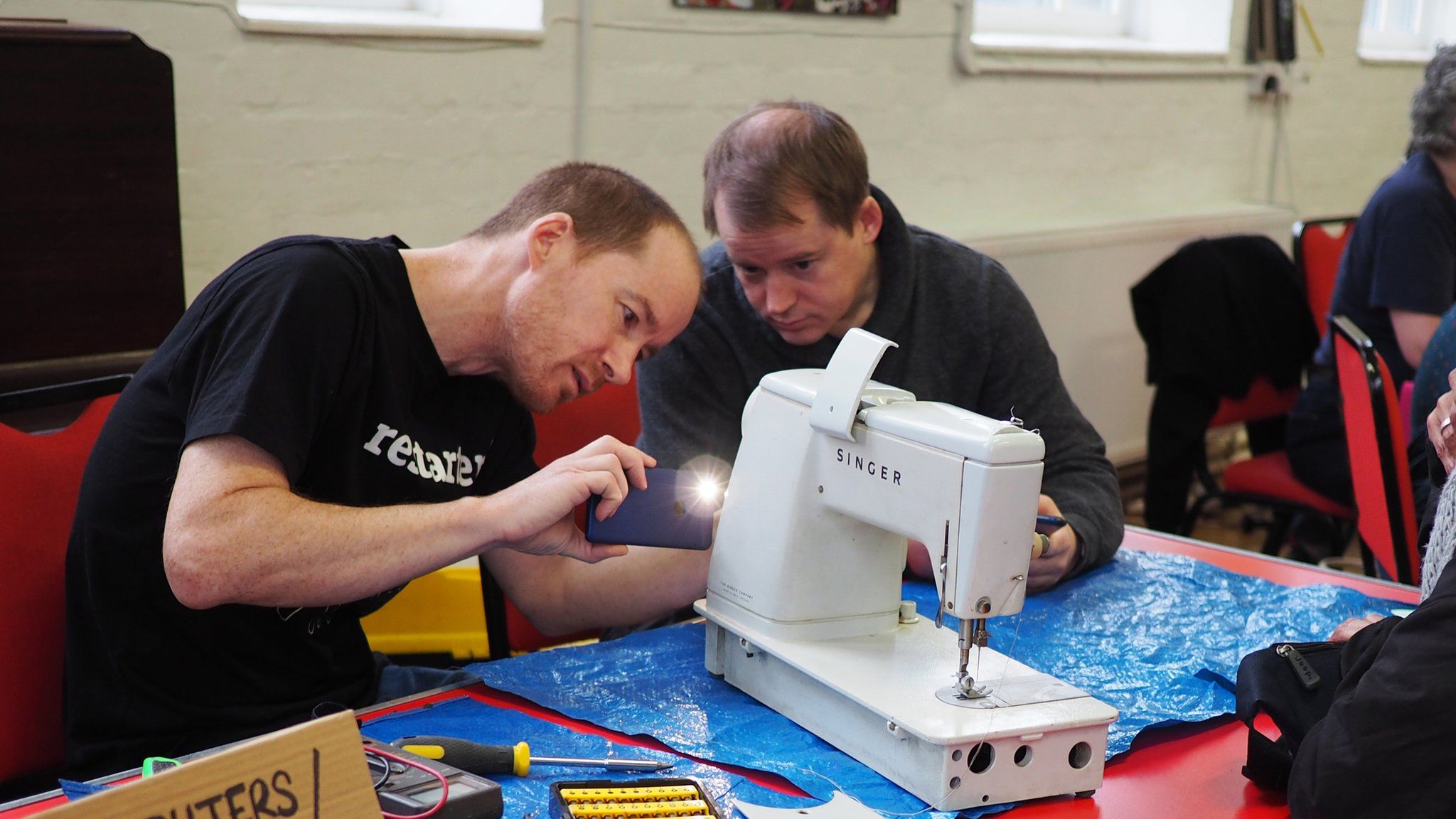 Two men with tools taking a look at a broken sewing machine