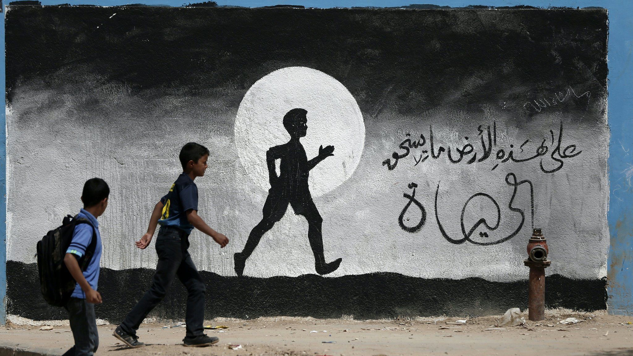 Two Palestinian schoolboys walk past a graffiti painted on a wall of the United Nations school of Beit Hanun, in the northern Gaza Strip, on May 9, 2016