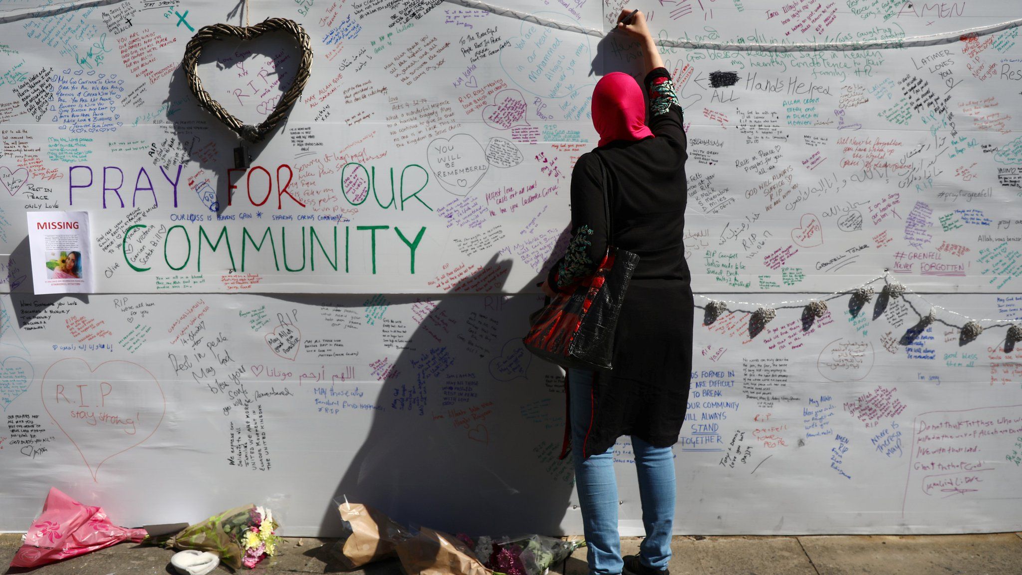 A woman writes on a message wall near to the Grenfell Tower block