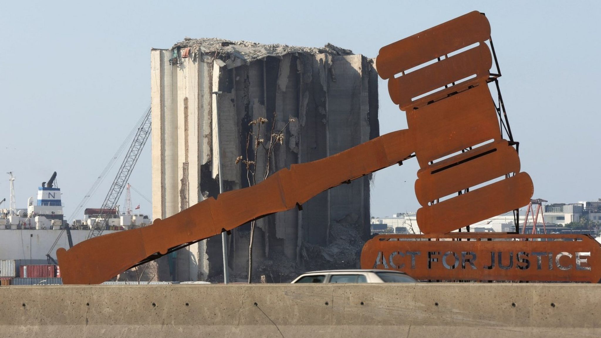Инсталляция с изображением судейского молотка и надписью «Действовать во имя справедливости» на стене напротив разрушенных зернохранилищ в порту Бейрута (24 января 2023 г.)