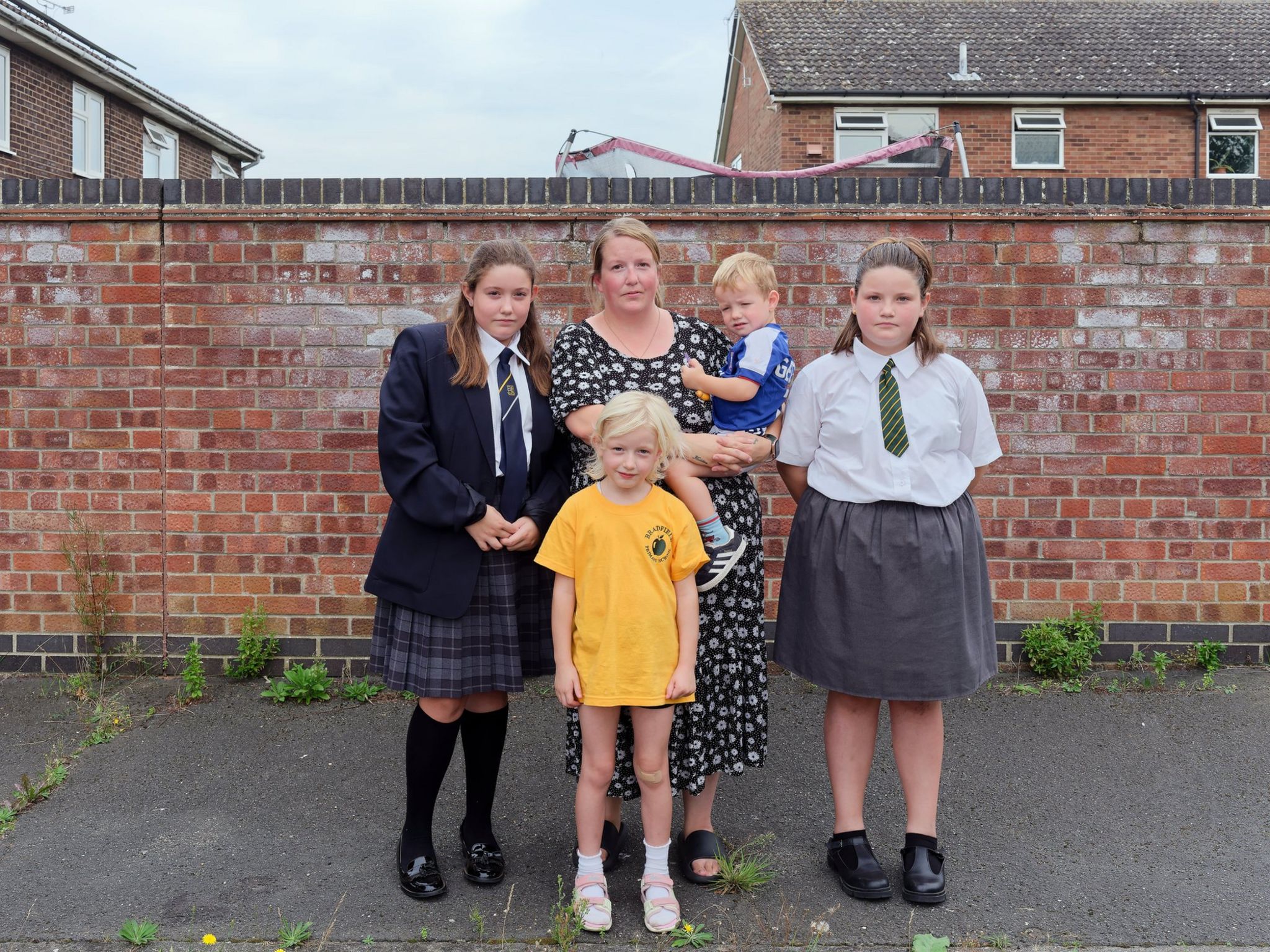 Jodie, pictured with all her four children, shown in front of a red brick wall with modern council-built terraced housing in the background