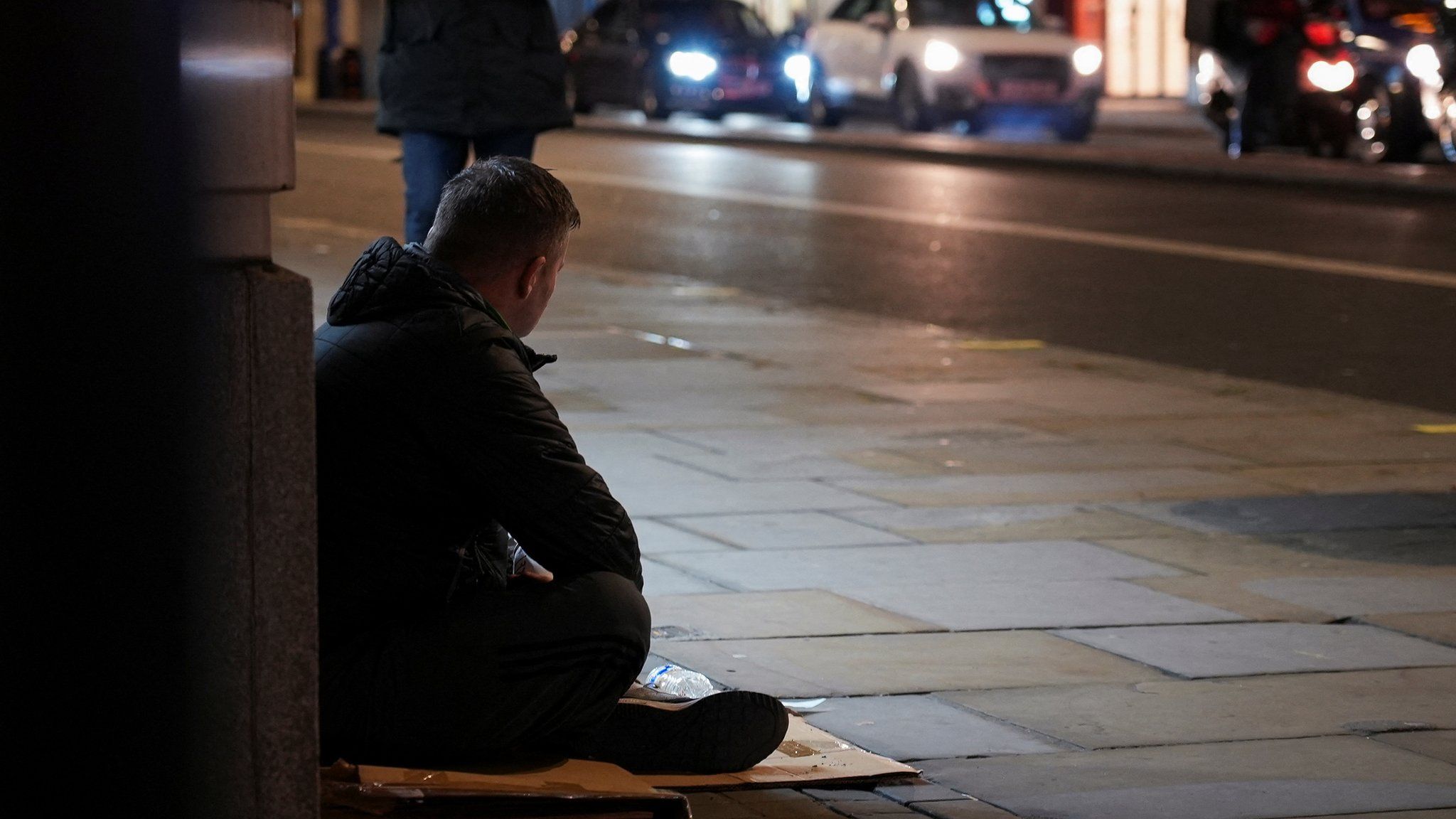 A homeless person on the street as cars pass by