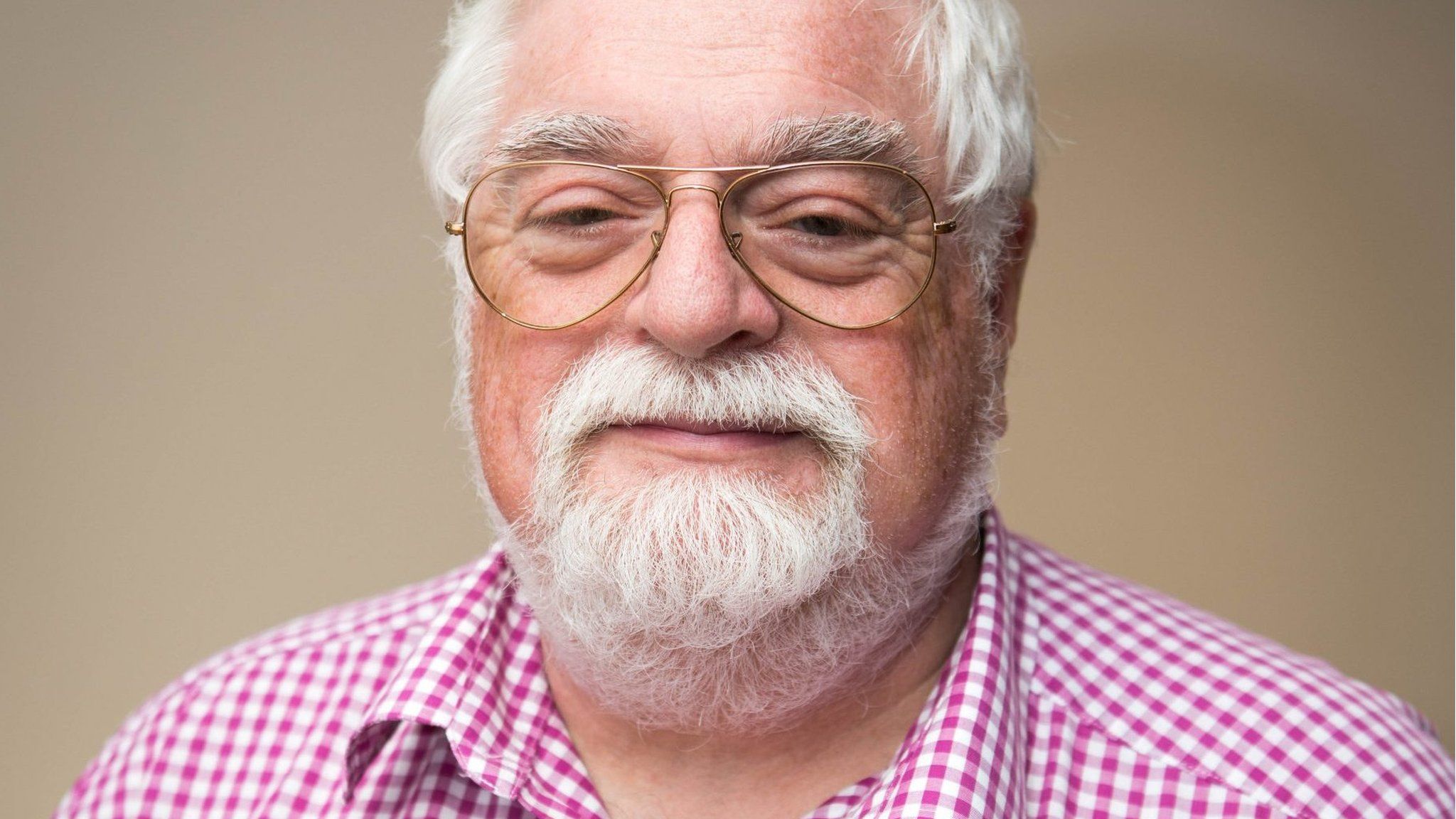 a white man with grey hair and beard and glasses and a pink checked shirt