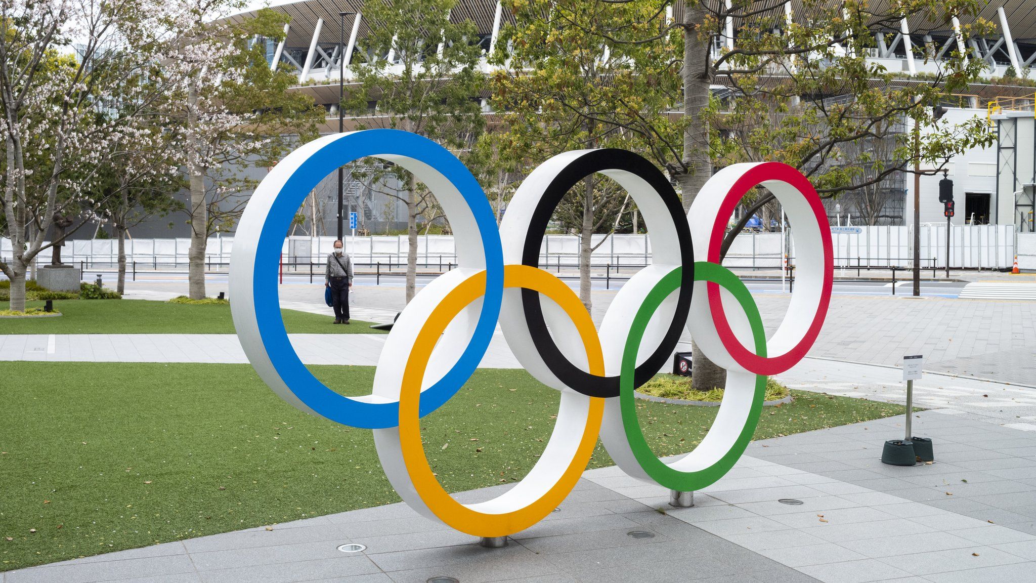 A man in a face mask stands behind a statue of the Olympic rings in Tokyo