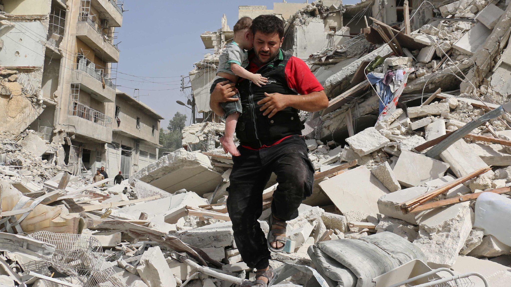 A Syrian man carries a baby after removing him from the rubble of a destroyed building following a reported air strike in the Qatarji neighbourhood of the northern city of Aleppo on September 21, 2016