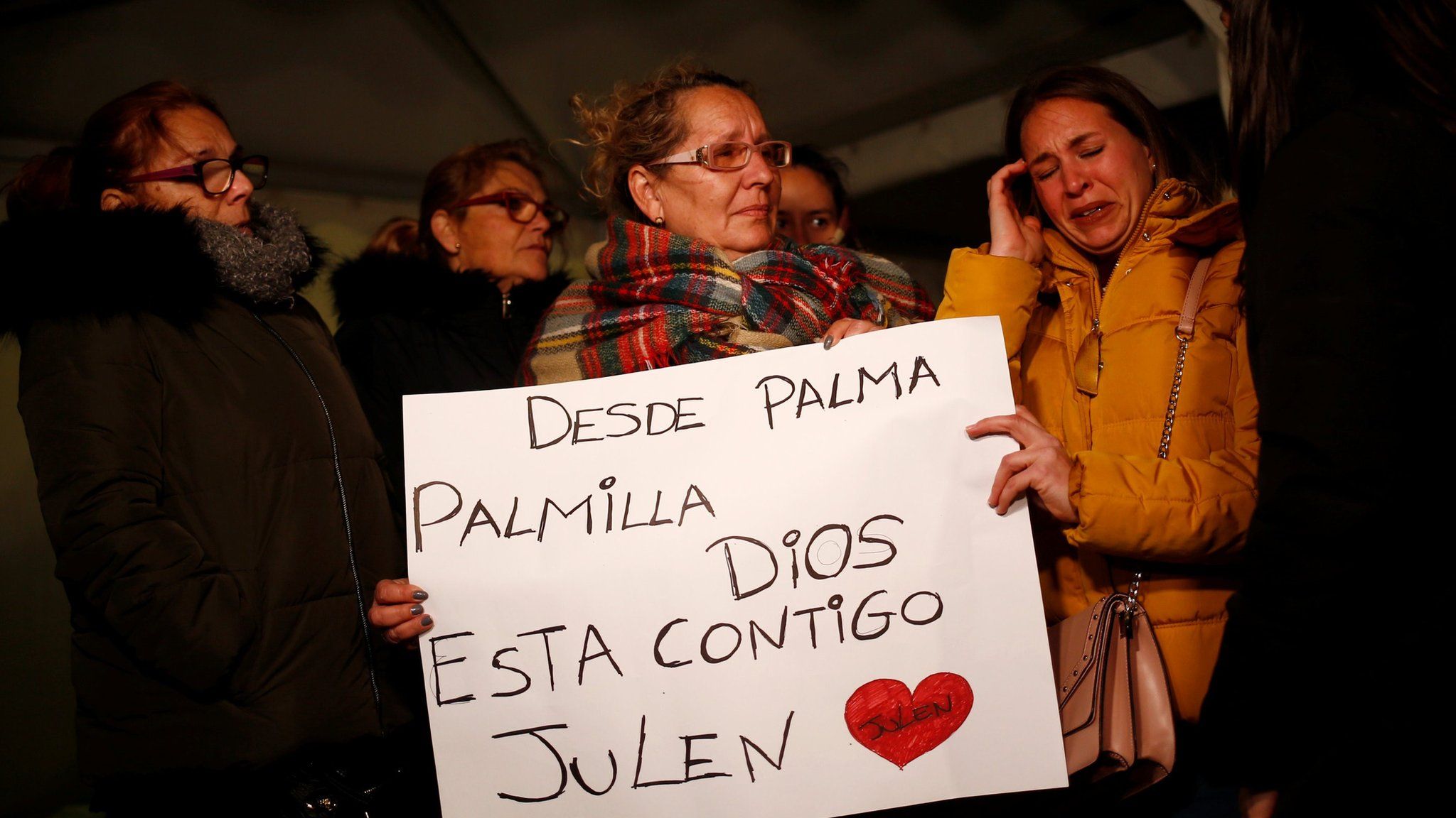 Women crying at a vigil on 24 January, holding a banner that reads: "From Palma Palmilla, God is with you, Julen"