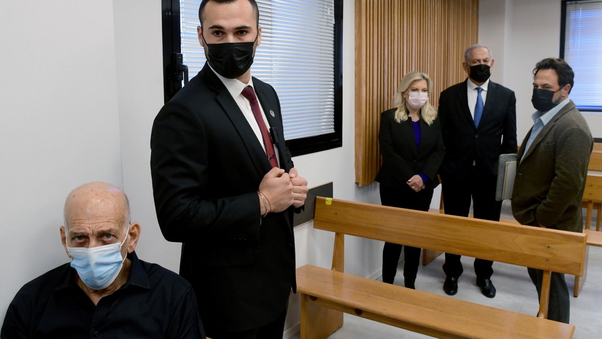 Ehud Olmert (L) sits inside the Tel Aviv Magistrate's Court, while Benjamin Netanyahu (2nd R) and his wife Sara (3rd R) stand behind him (10 January 2022)