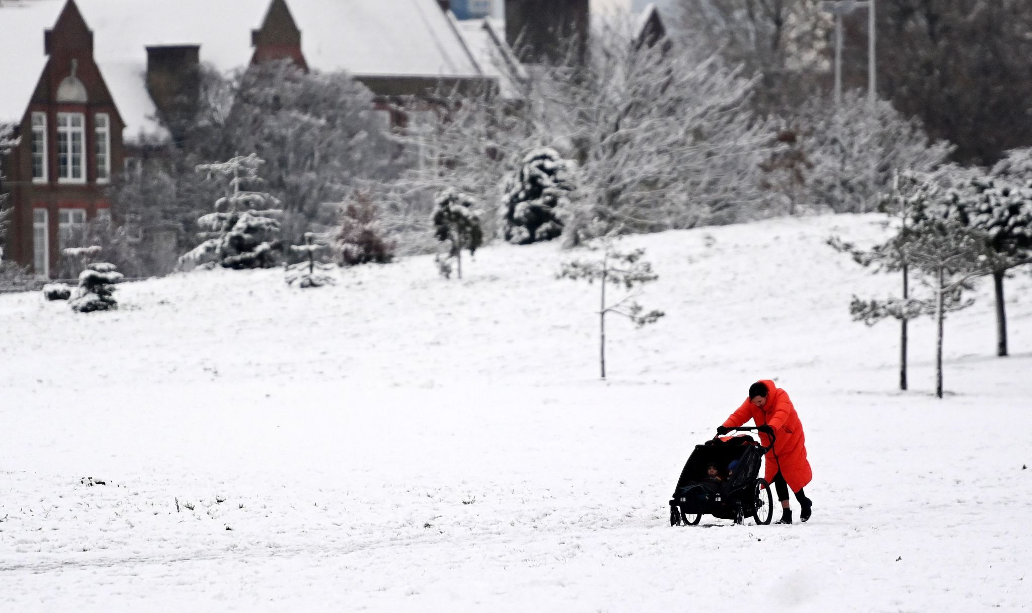 A woman pushes her child through a snow covered park in central London