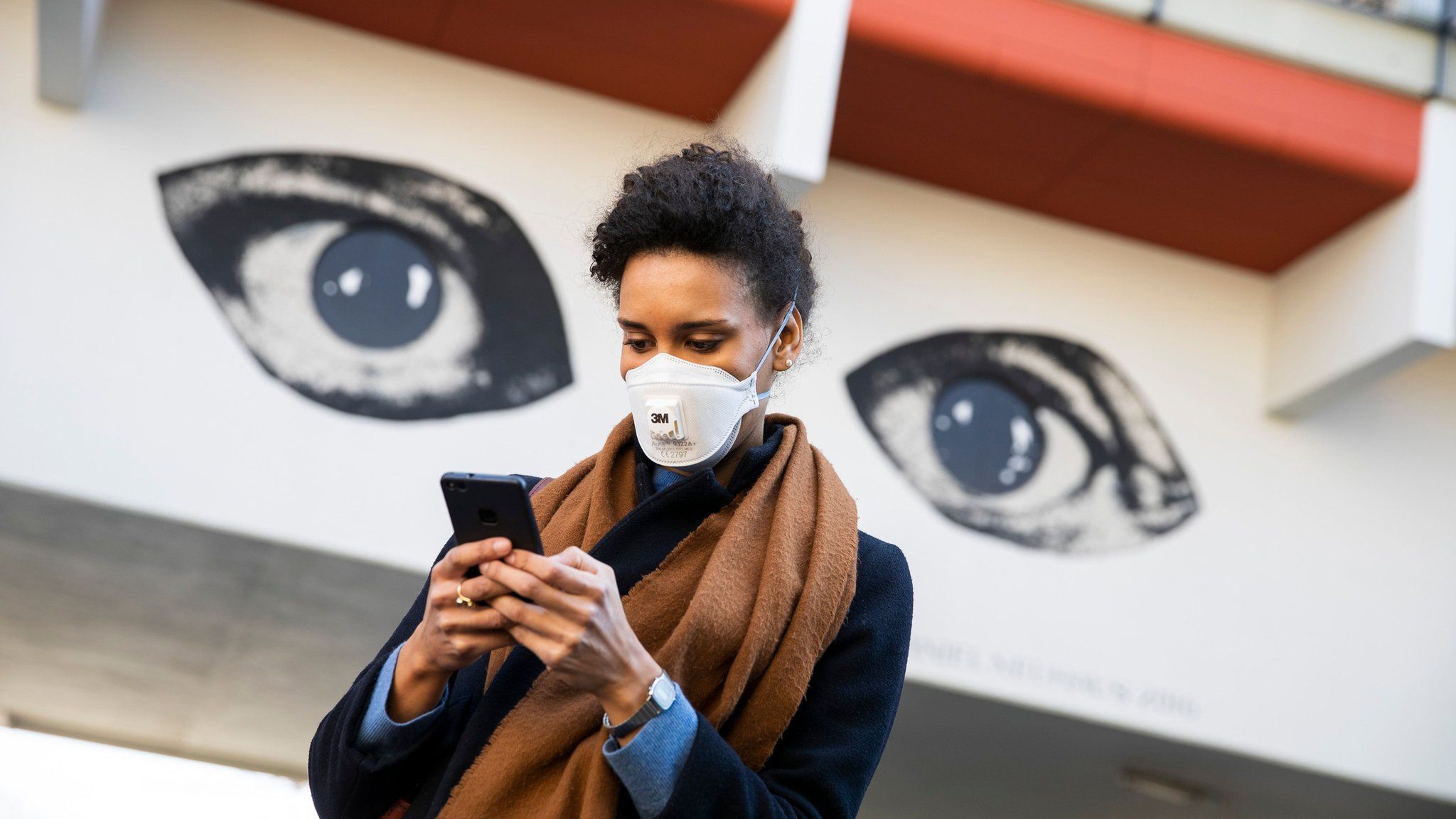 Woman using smartphone by graffitti of two eyes