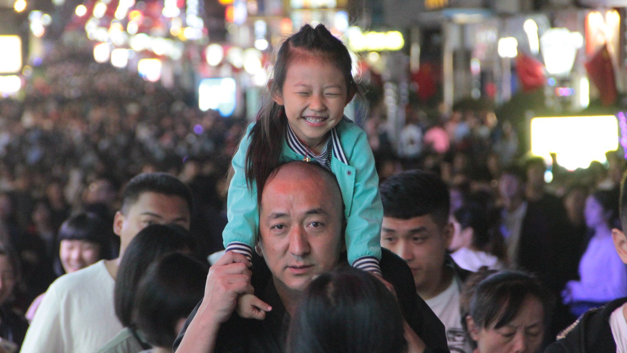 A girl rides on her father's neck at Taidong Pedestrian Street in Qingdao, Shandong, 5 October 2018