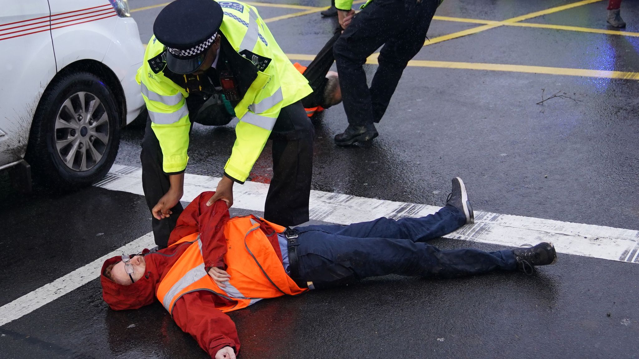 A police officer detains an Insulate Britain protester occupying a roundabout leading from the M25 motorway to Heathrow Airport