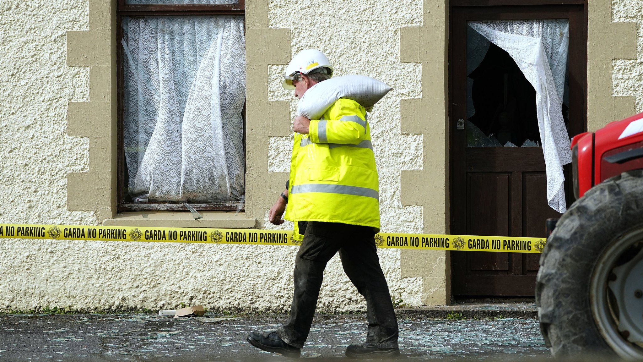 A man carries a sandbag over his shoulder outside a house in Creeslough that has had its windows blown out by the explosion