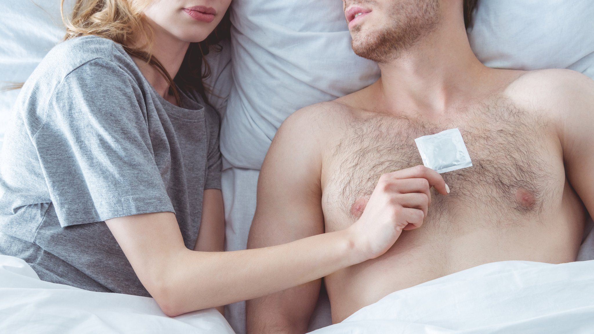 Man and woman in bed, woman holding condom