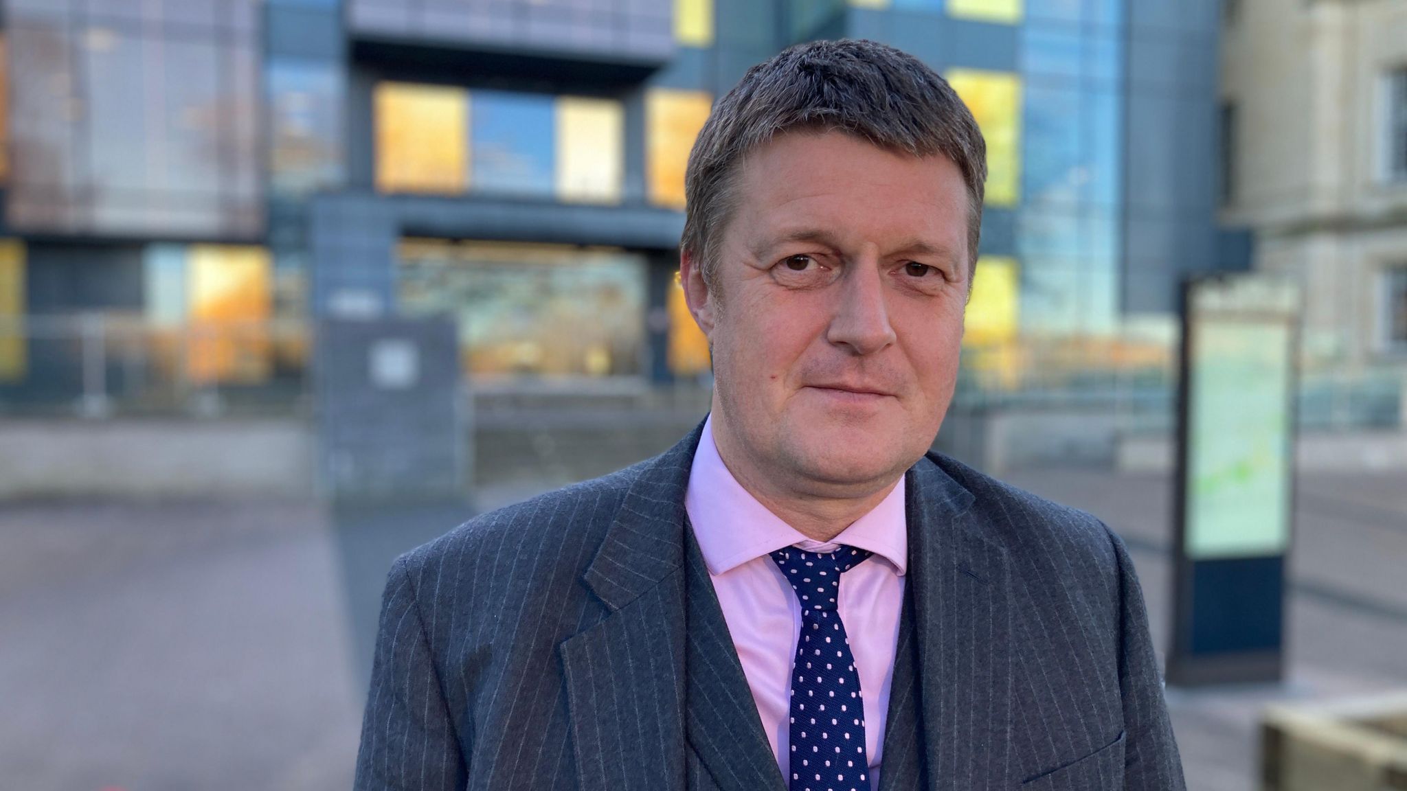 Richard Clewer, pictured wearing a dark three-piece suit, pink shirt and tie. 