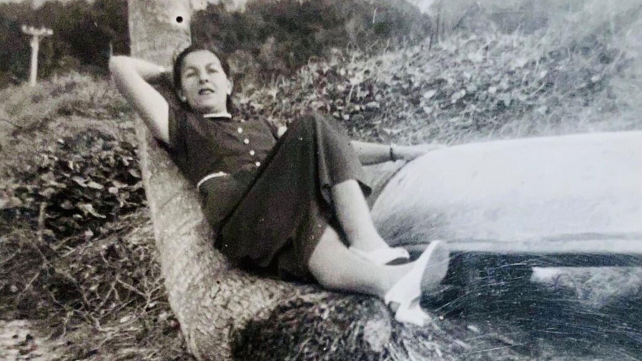 Black and white photo of Phyll Babb as a young woman , lying in a tree's roots in jamaica