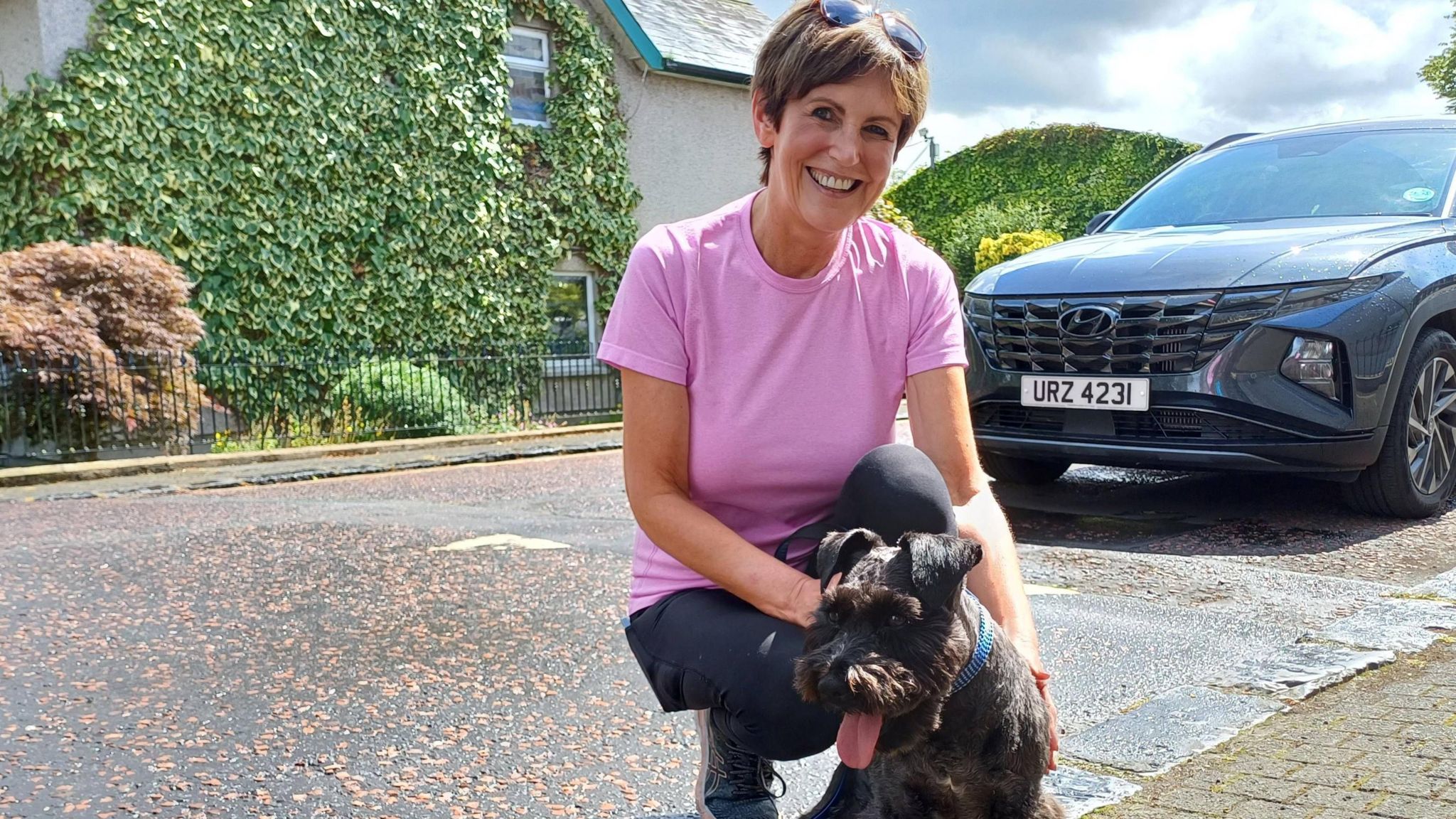 Julie is posing with her dog. She's wearing a pick top.