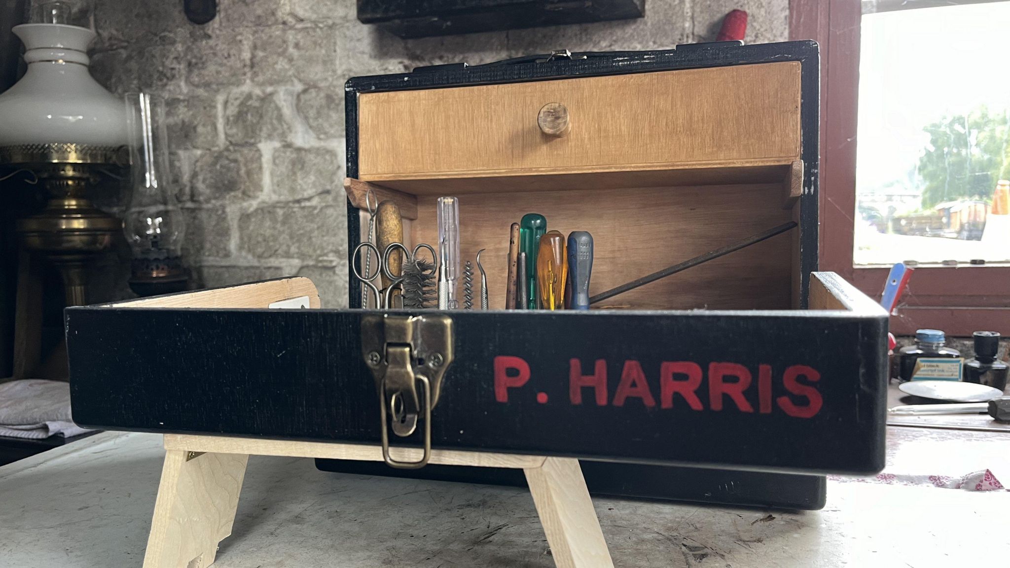 A black wooden toolbox with red letters that reads "P HARRIS". It is open and tools, including scissors and screwdrivers, are visible.