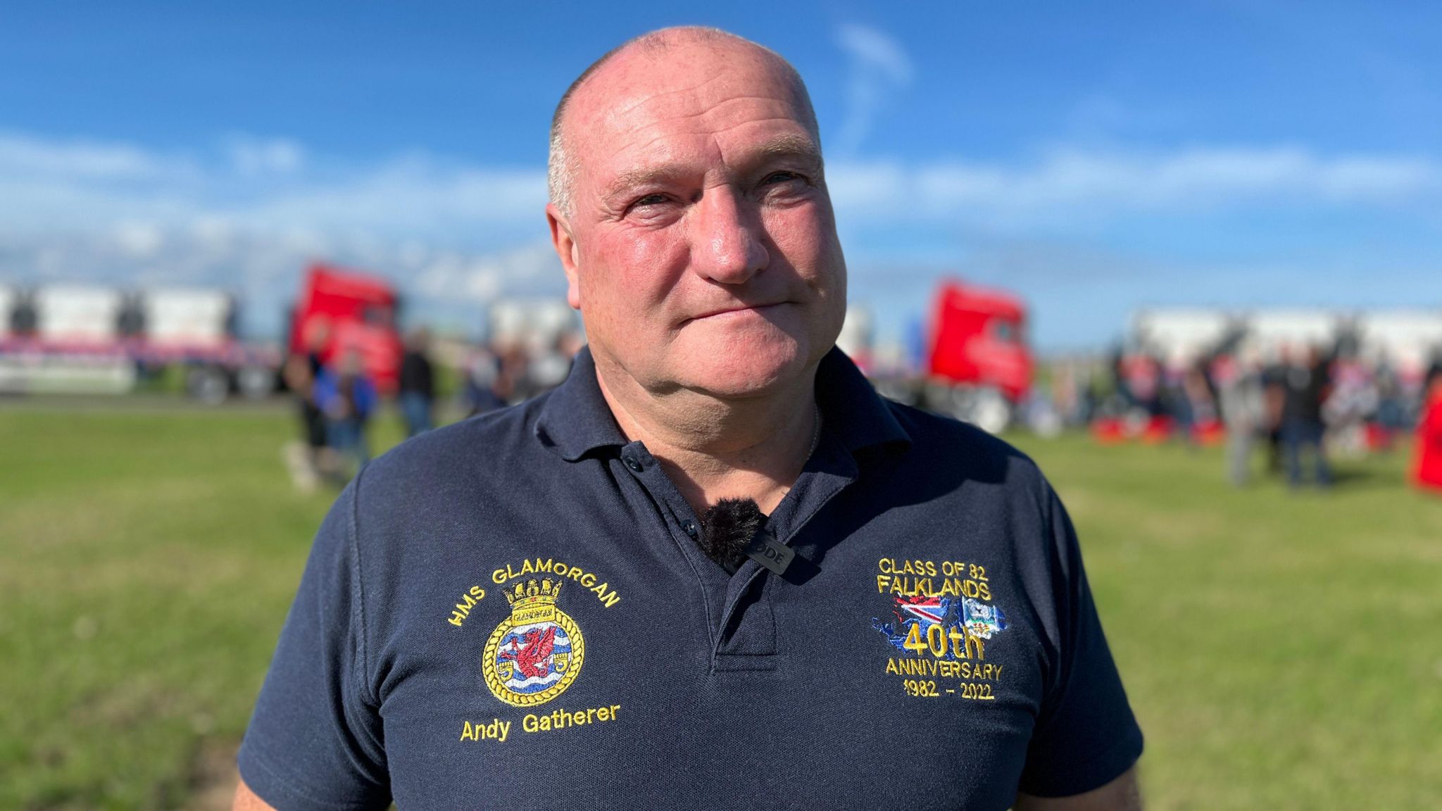 Andy Gatherer, stood in front of the statues, he is wearing a t-shirt which has badges and recognition of his service