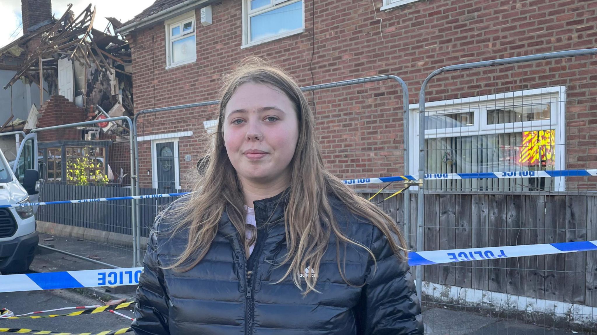Rebekah Ashcroft in black jacket with the damaged house and a police tape in the background