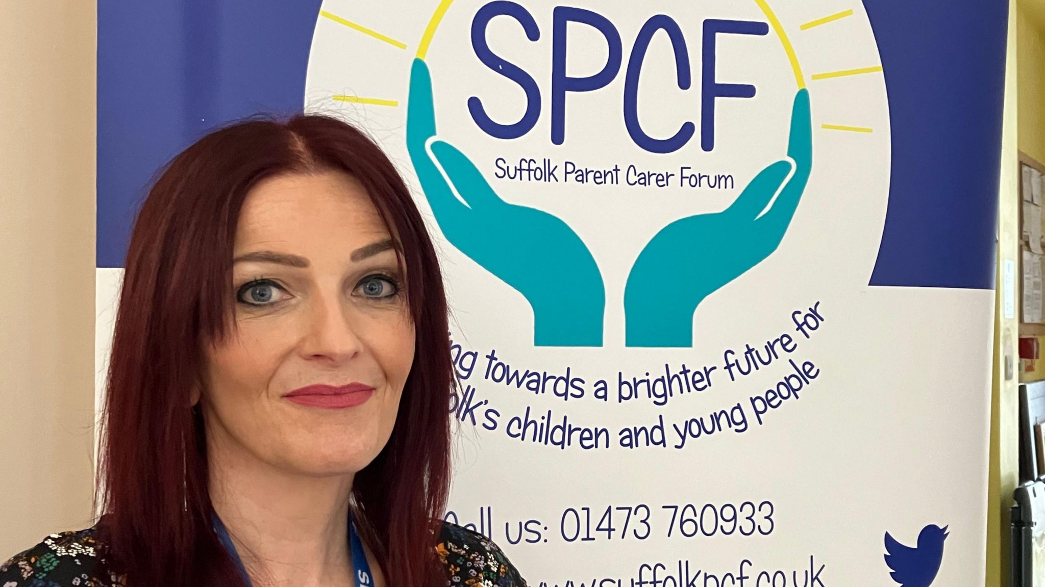 Person with carmine-coloured hair standing in front of sign saying Suffolk Parent Carer Forum