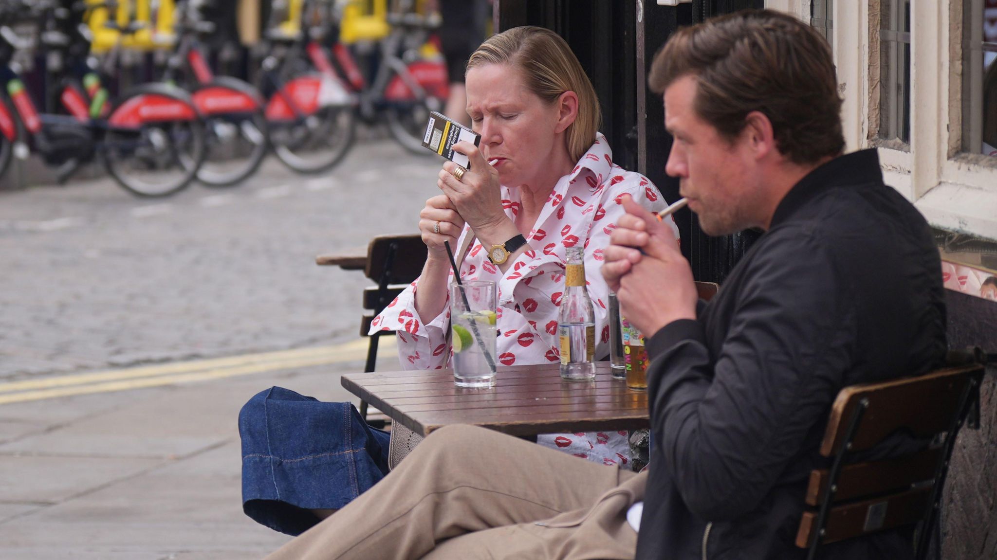 Customers light up cigarettes while sitting outside a pub in Soho, London