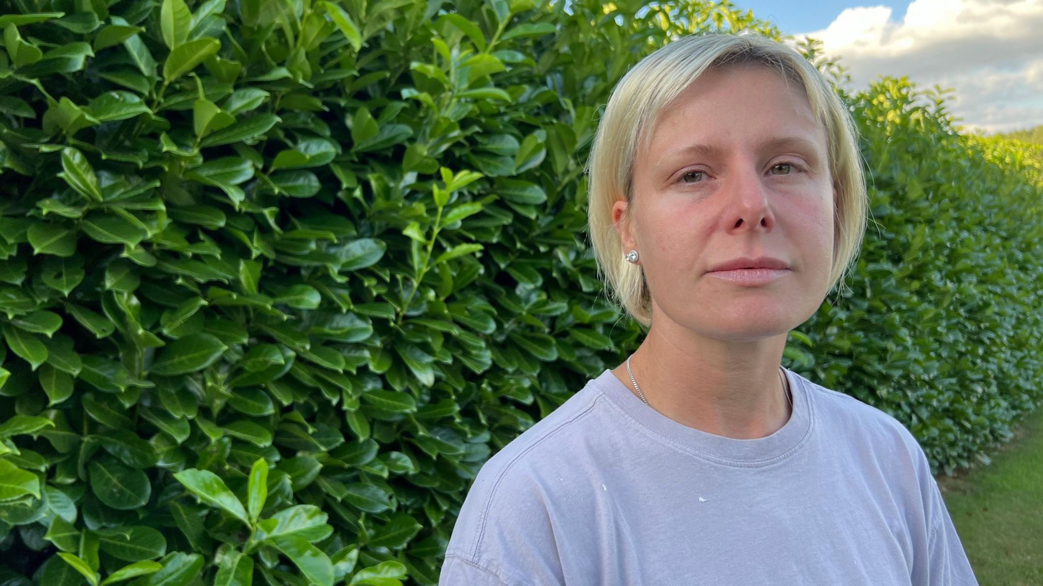 Kirsty is pictured in her garden in front of a hedge wearing a grey t-shirt