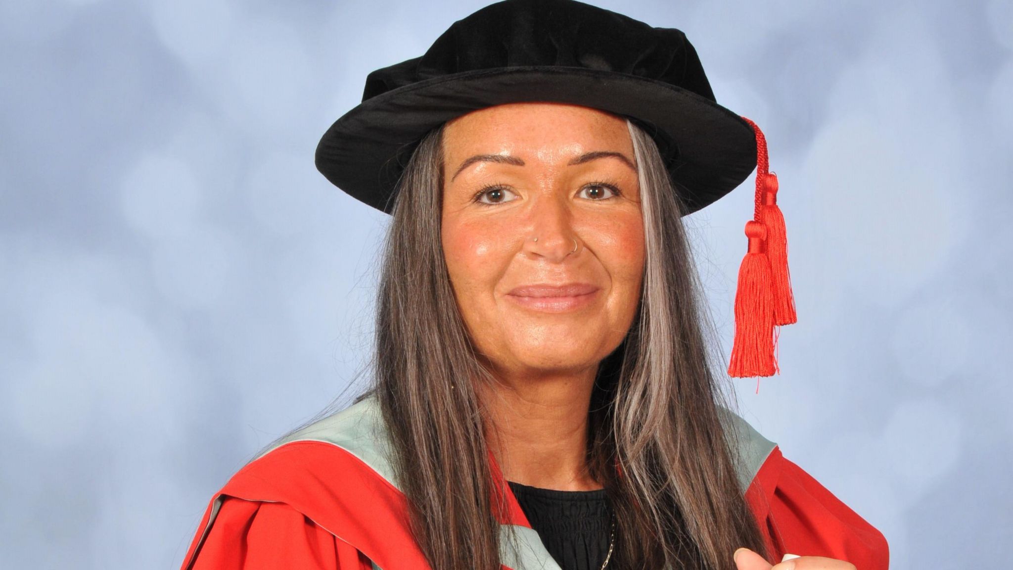 Sarah wearing red and mint green gown with a black cap and holding a scroll in the right hand