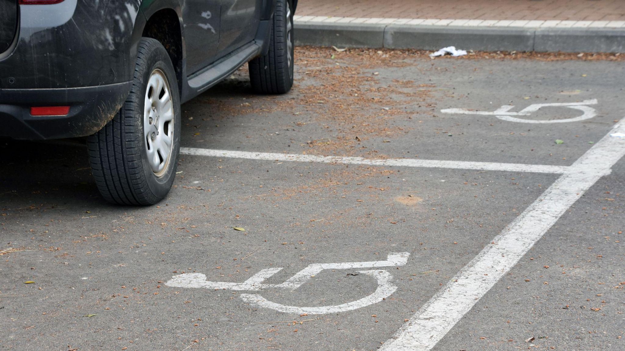 A car is parked across two disabled parking spaces