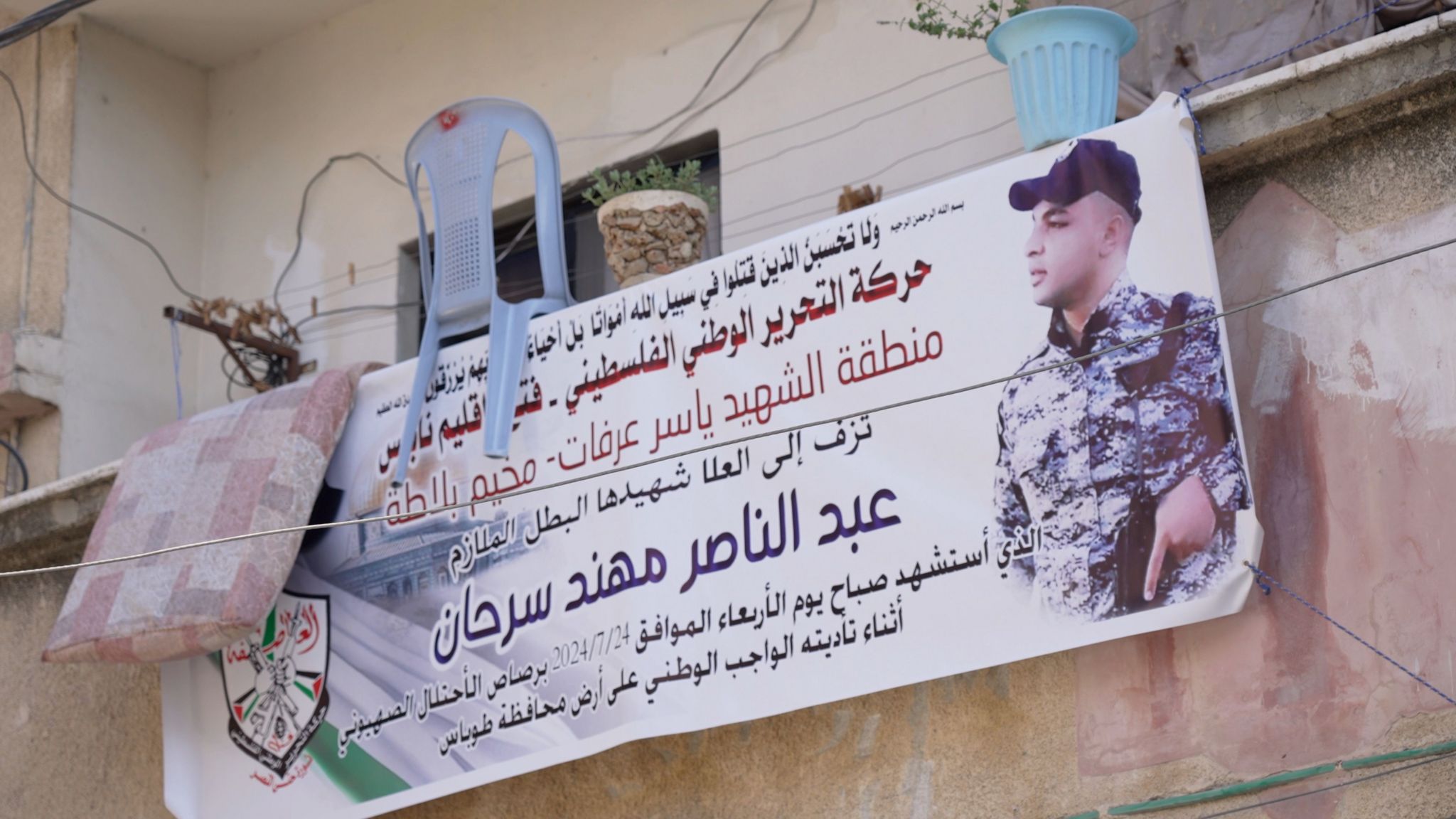 A poster hanging on a balcony shows Arabic text and a picture of a killed young man