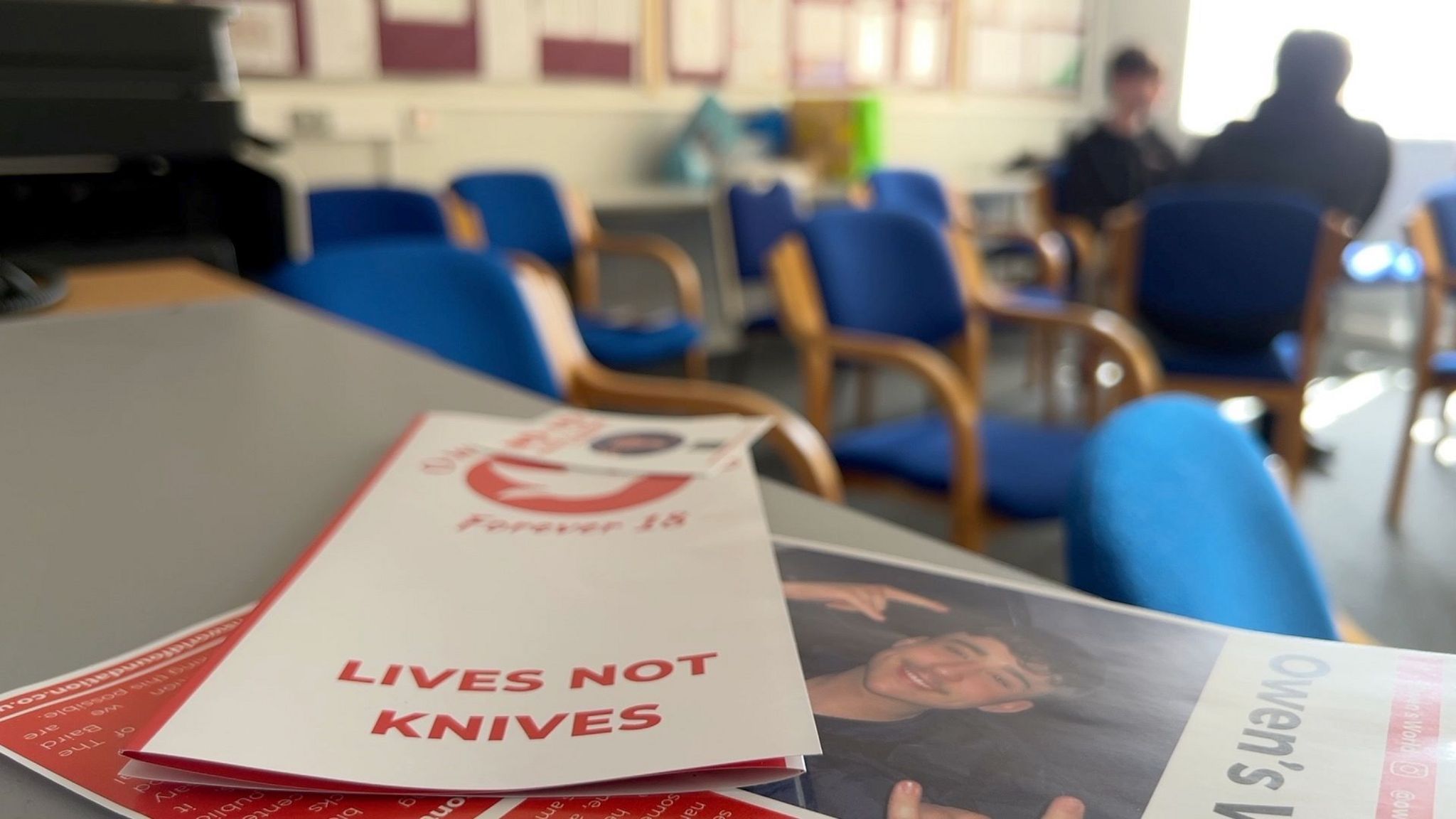 Owen's World flyers on a table branded in red and white with school seats in the background