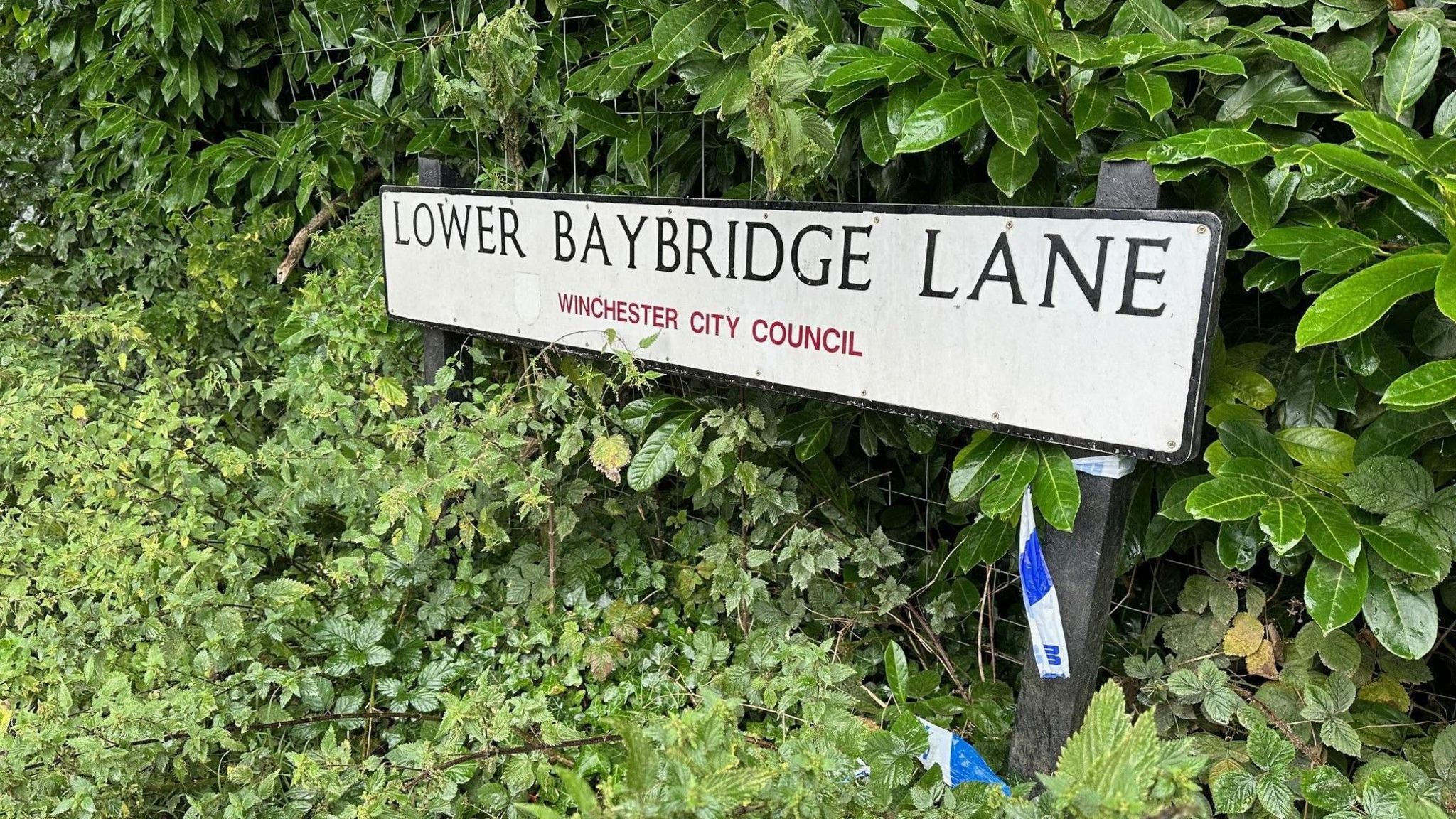 Police tape can be seen around the road sign for Lower Baybridge Lane.