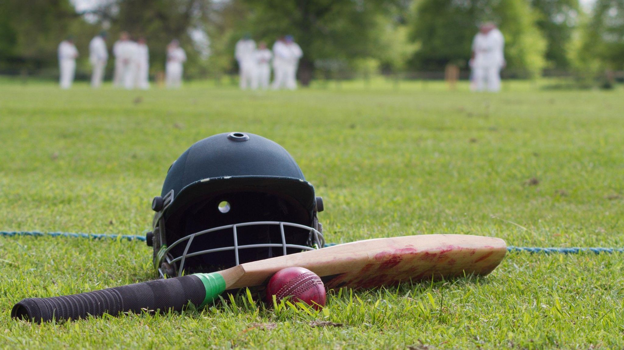 A cricket helmet, bat and ball on a cricket pitch  