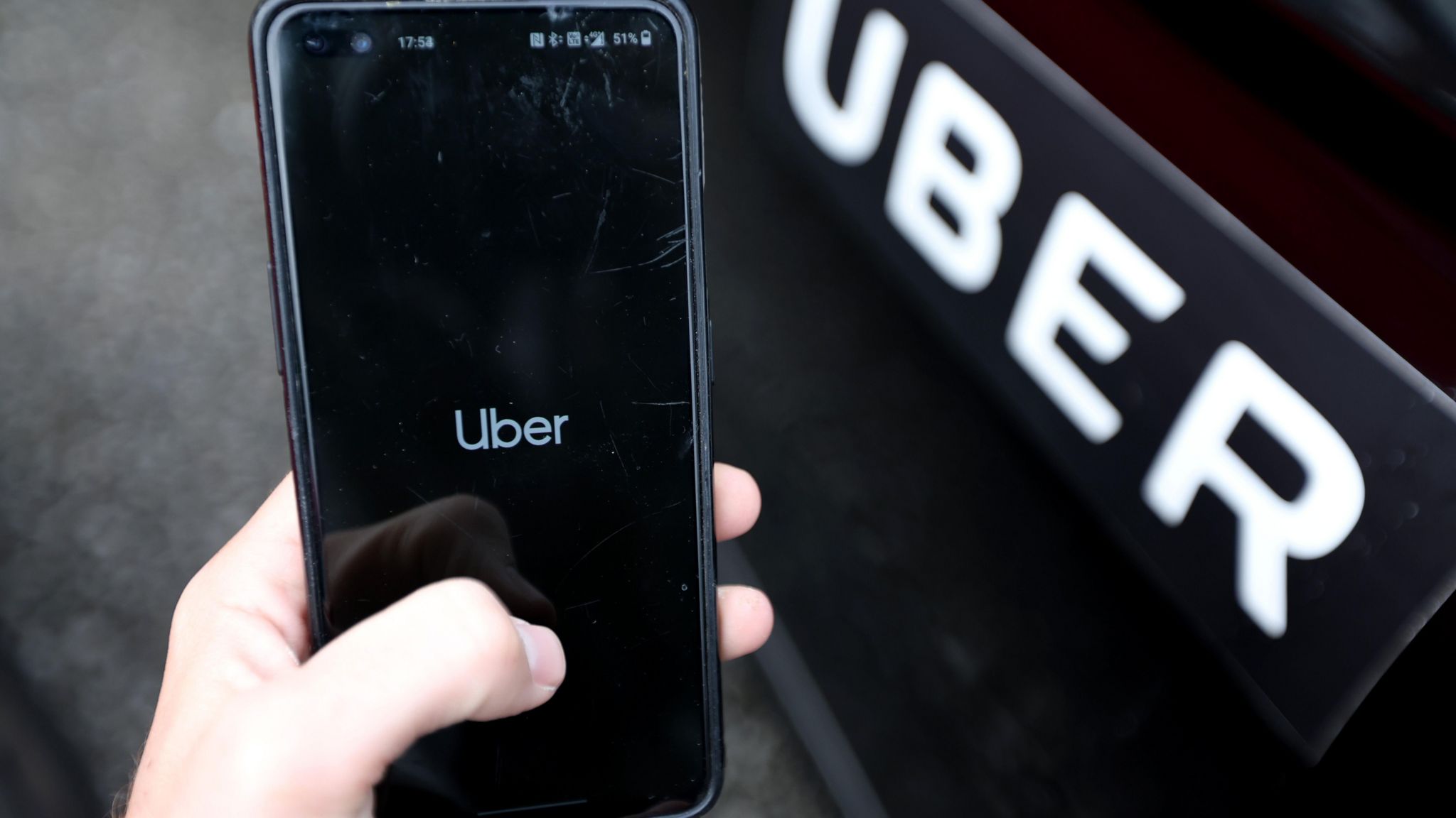 Uber app on a phone next to an Uber branded car