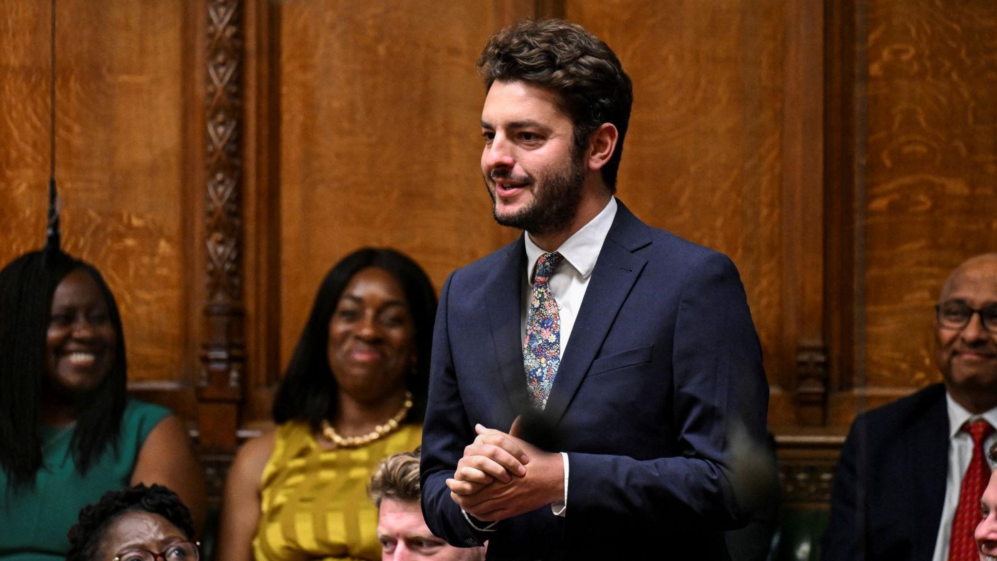 Jack Abbott wearing a suit and patterned tie speaks from the back benches in the House of Commons, with his hands clasped together