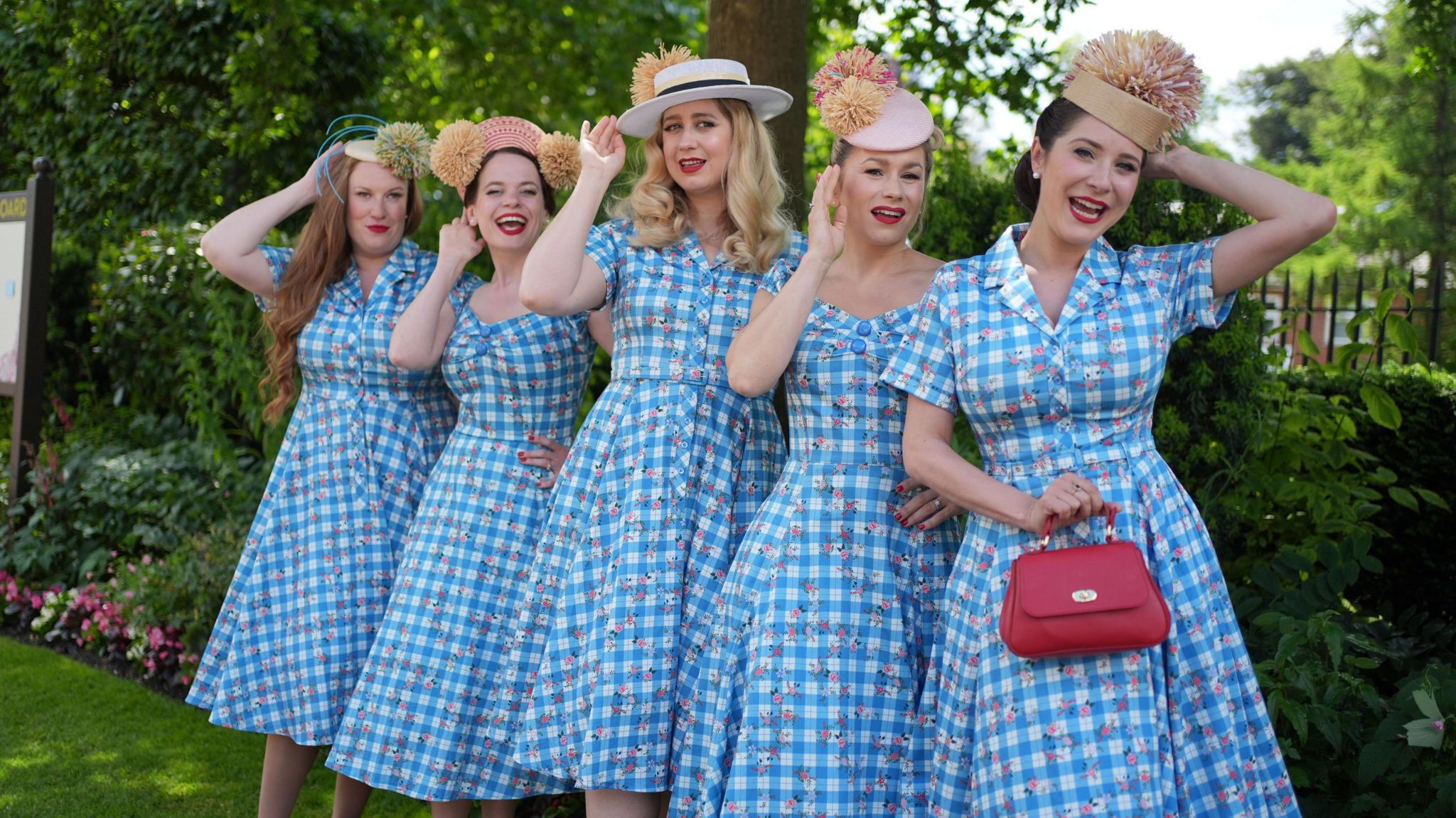 A group of five women line up and pose for the camera wearing matching blue and white gingham check dresses