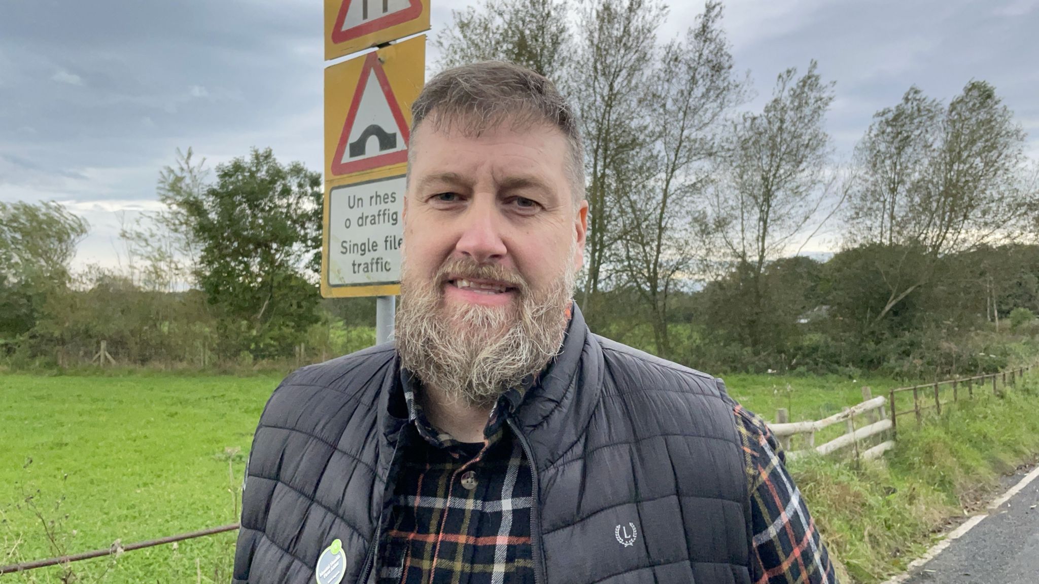 Councillor Chris Evan stood in front of a sign warning of single file crossing over Llanerch bridge - prior to the bridge being completely destroyed