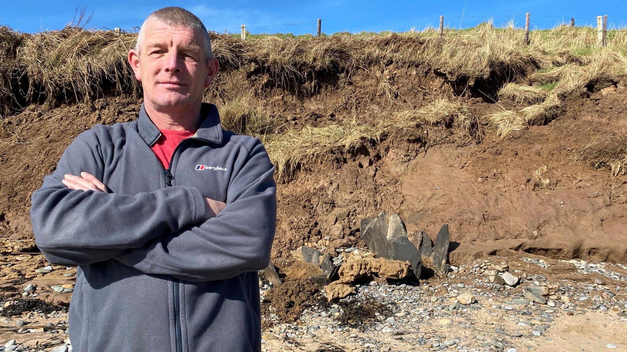 Craig Thompson, with his arms folded standing in front of a collapsed cliff 