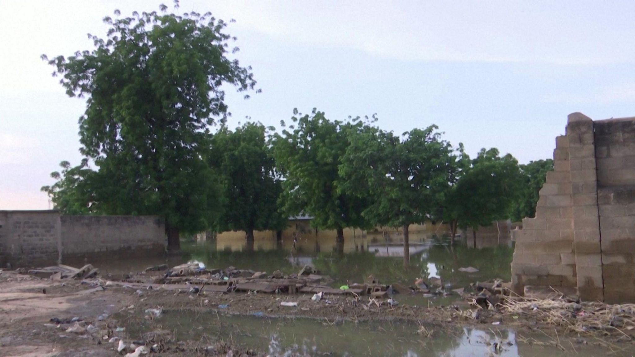 The collapsed wall of a compound near floodwater