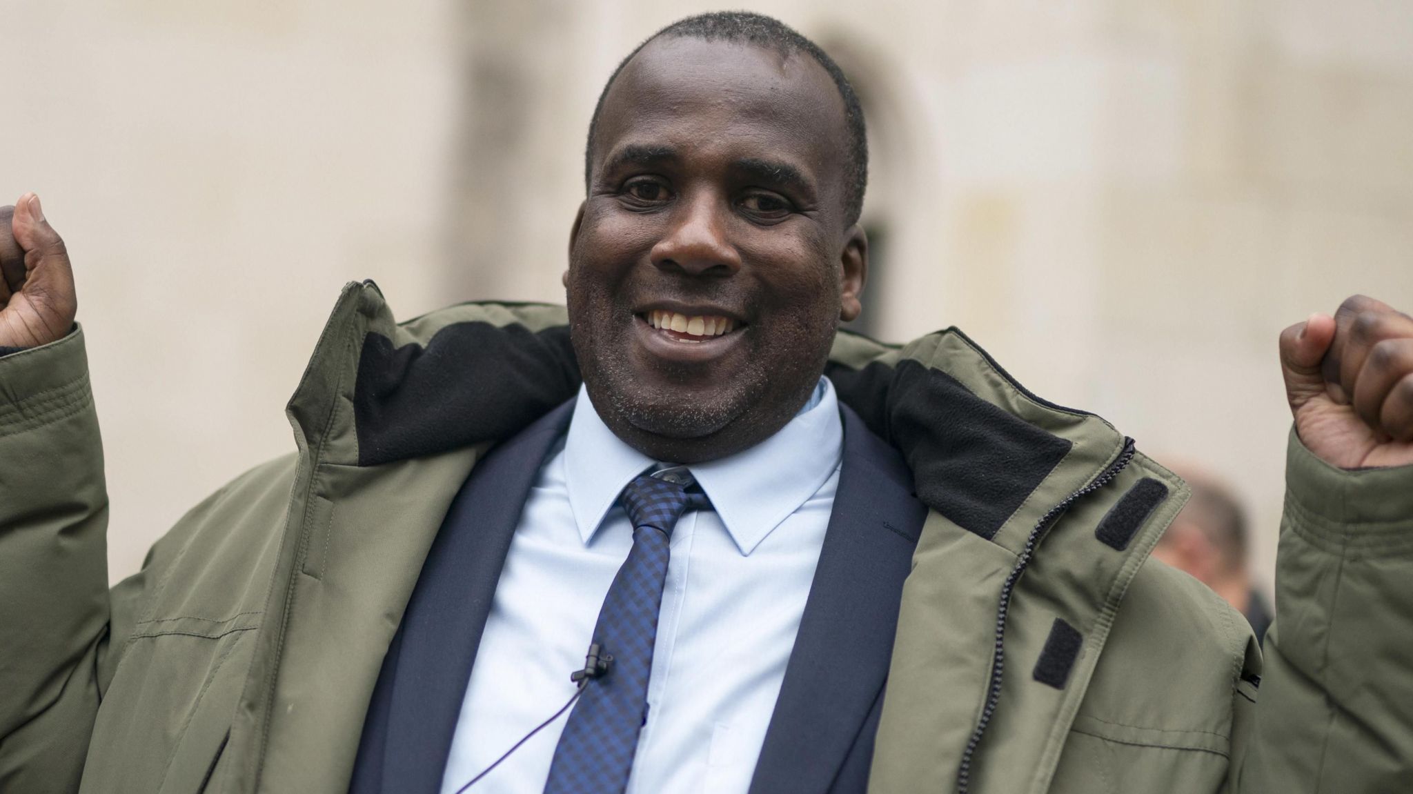 Oliver Campbell smiling outside court dressed in a blue suit and olive green jacket.