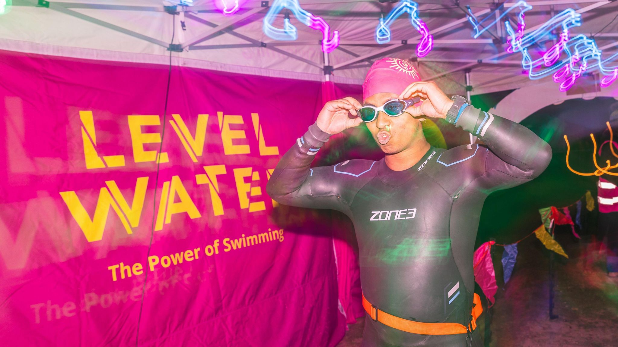 A swimmer puts their goggles on in front of a level water sign