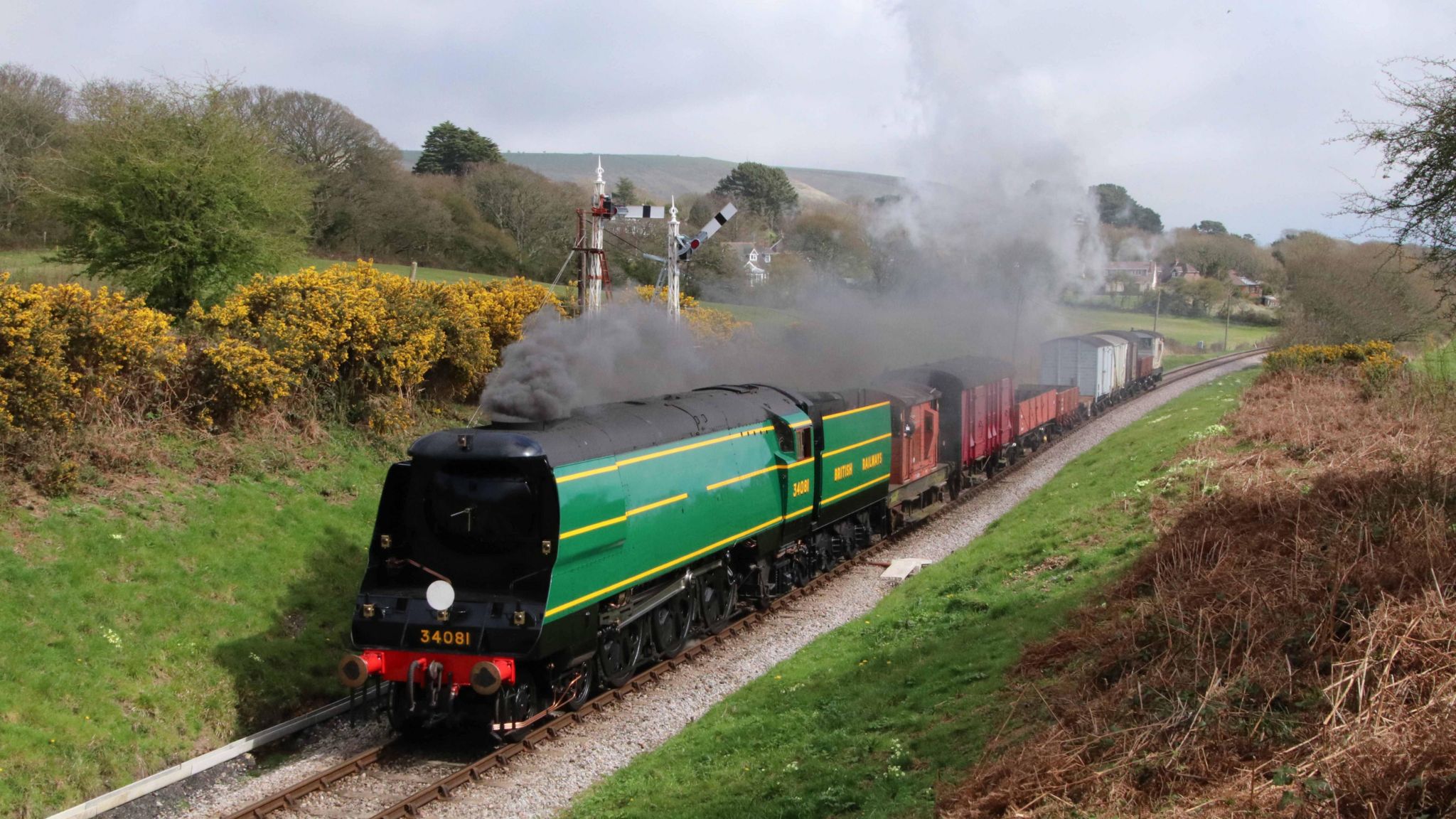 Green 1940s Bulleid Pacific class steam locomotive on a railway track with smoke pouring out in the countryside