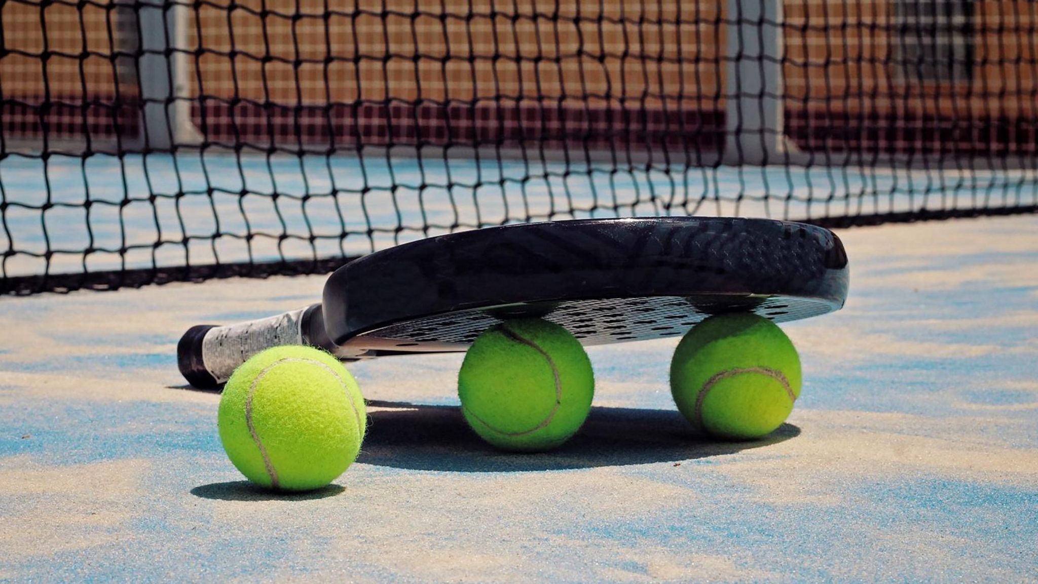 A padel racquet and balls on the floor next to a net