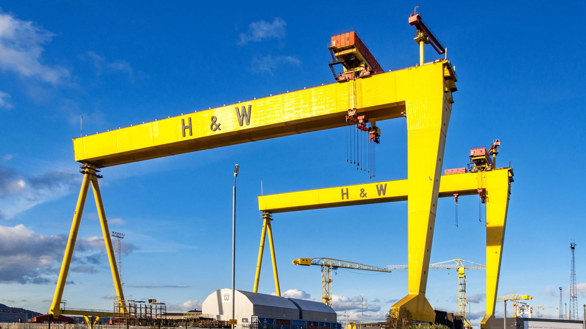 Twin shipbuilding gantry cranes in Titanic quarter. They are both yellow with H&W in black lettering printed across the top. The sky is very blue.