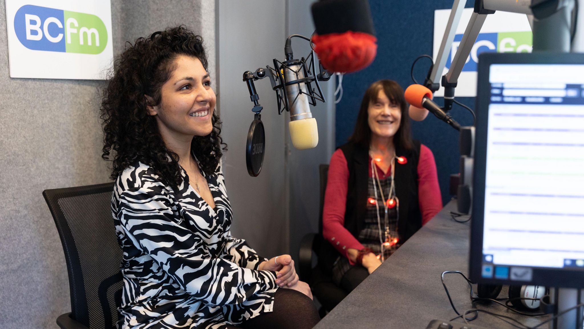 Two women sitting in front of microphones in a radio studio