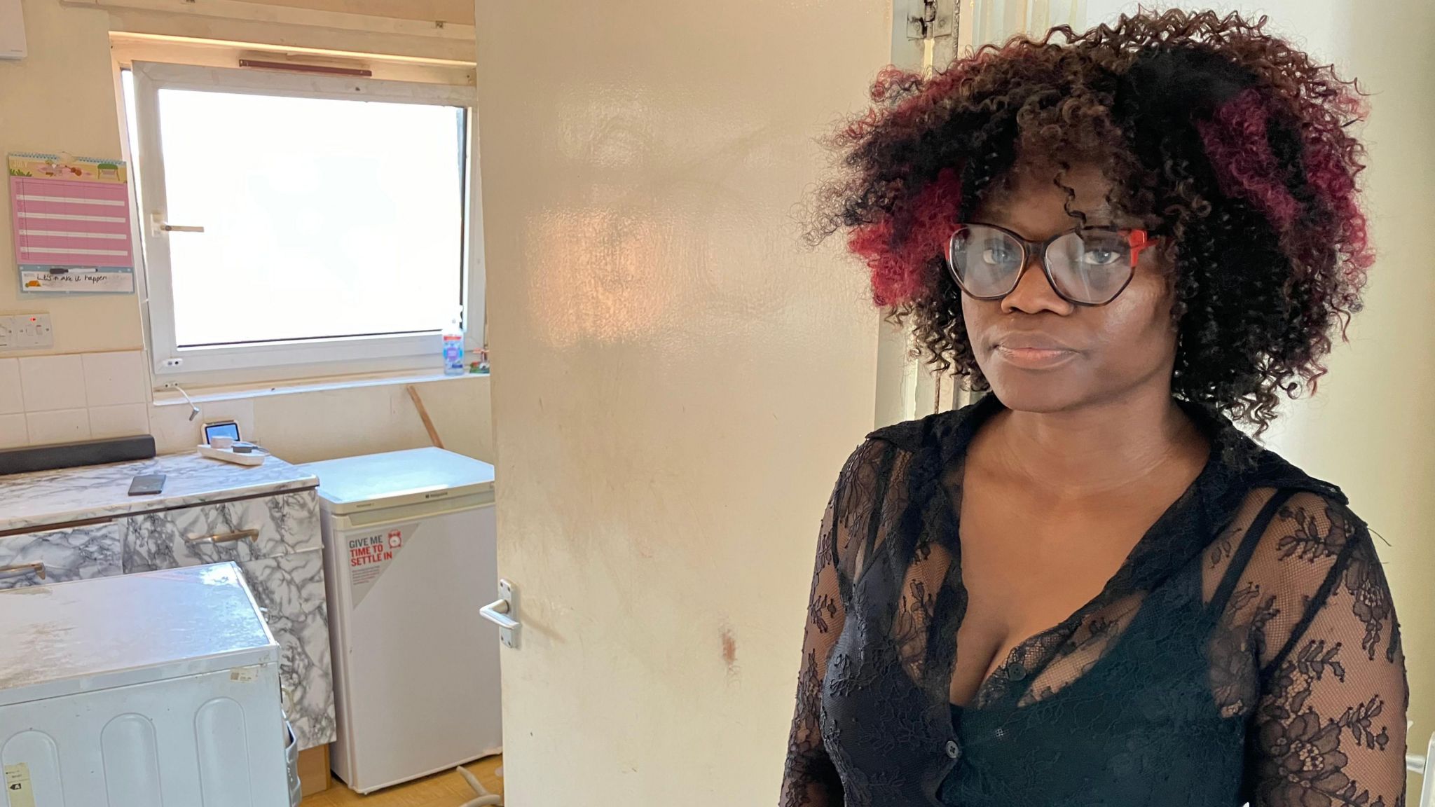 Woman with black curly hair and glasses stands in kitchen doorway