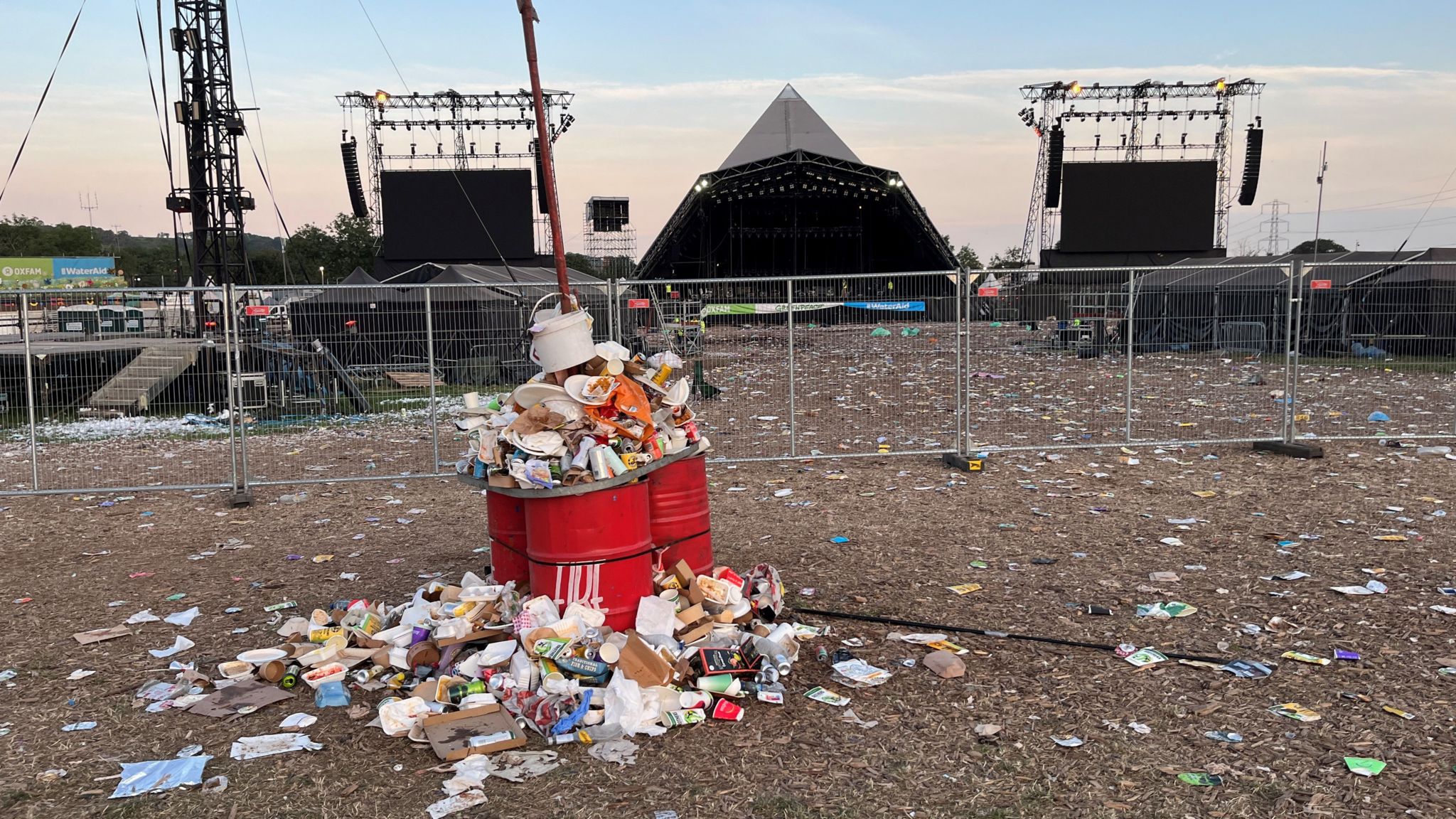 A red bin with rubbish overflowing next to the Pyramid stage at Glastonbury